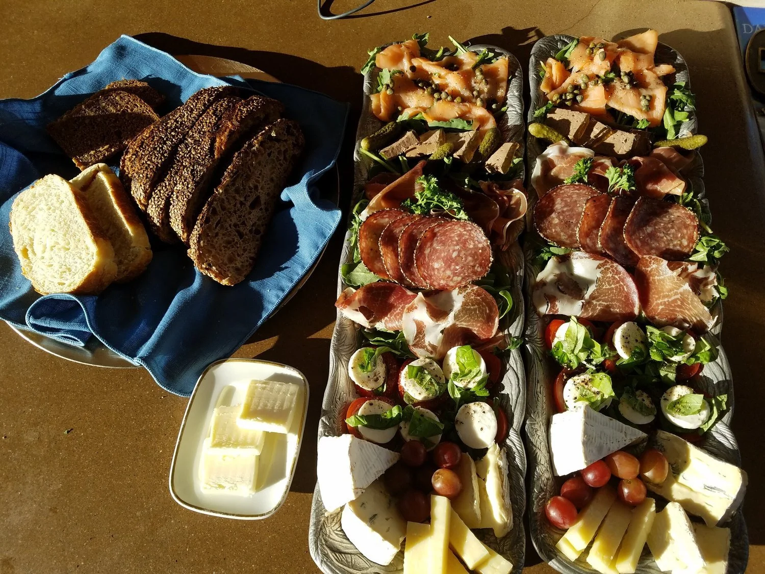 Cheese, bread, and an assorted charcuterie platter with meats, cheeses, grapes, cherry tomatoes, and vegetables.