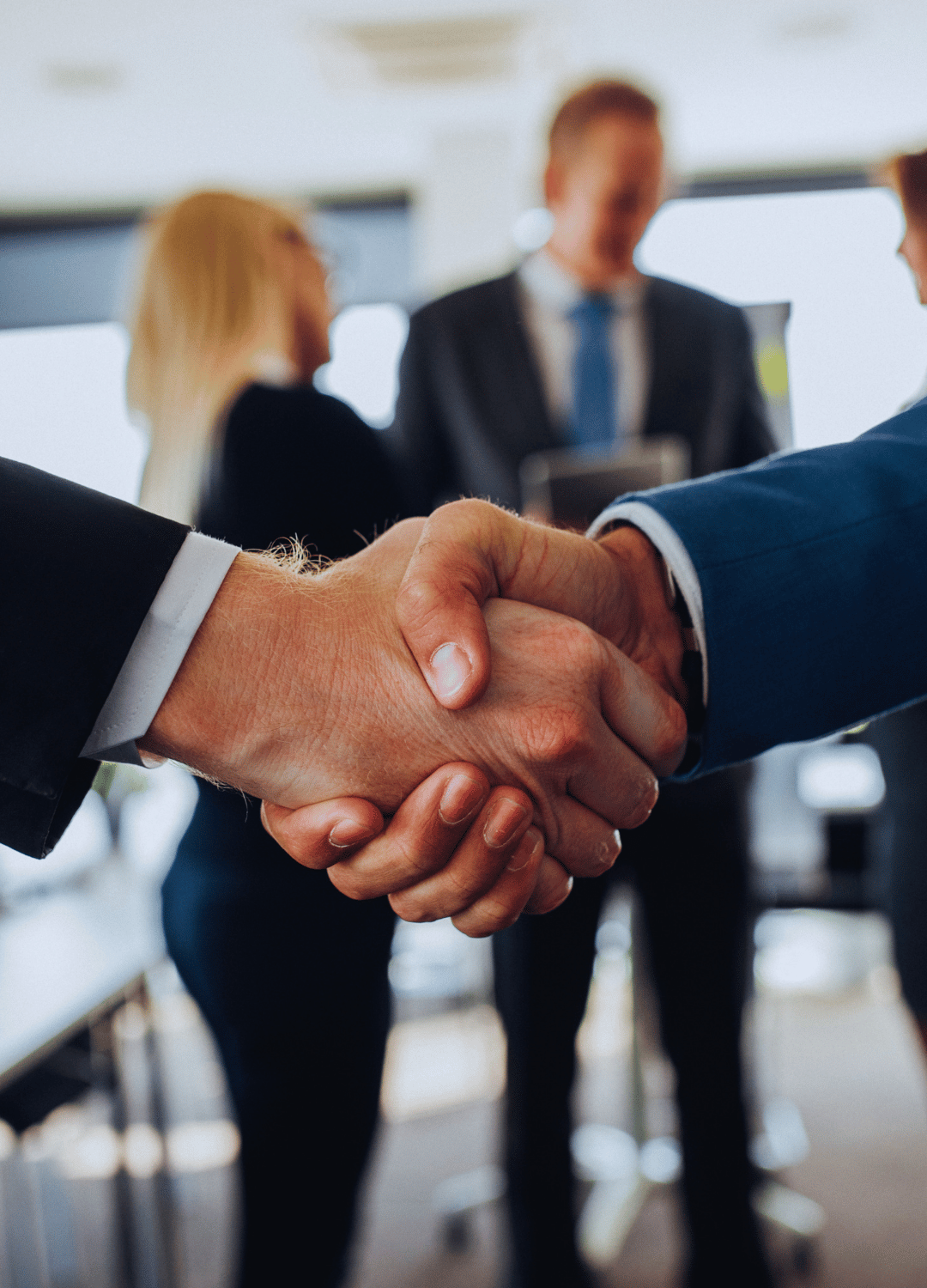 Close-up of two men shaking hands in a business meeting with blurred people in the background.