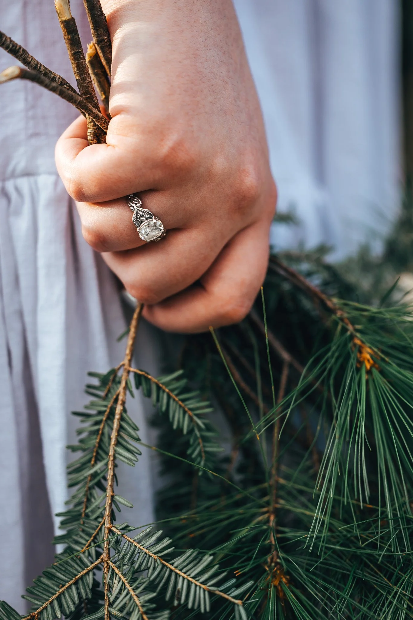Close-up of a person's hand holding pine branches, wearing a large diamond ring on the finger.