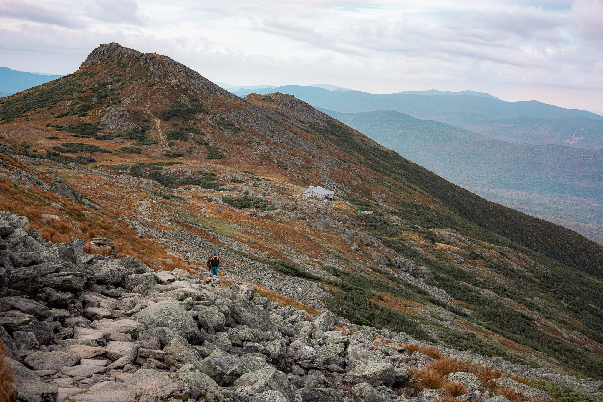 Hikers walking on rocky mountain trail with a mountain landscape and clouds in the background