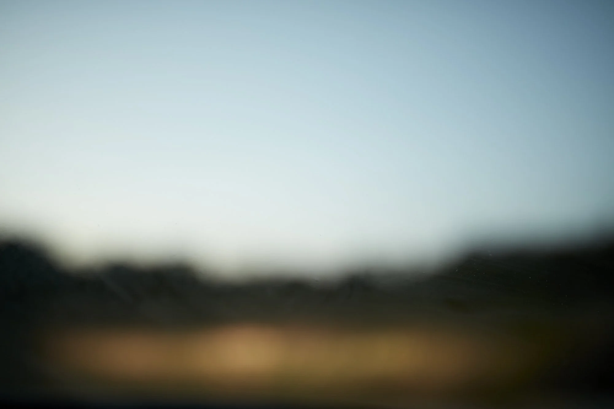 Blurred image with a gradient of colors from light blue at the top to dark at the bottom, resembling an out-of-focus landscape or abstract background.