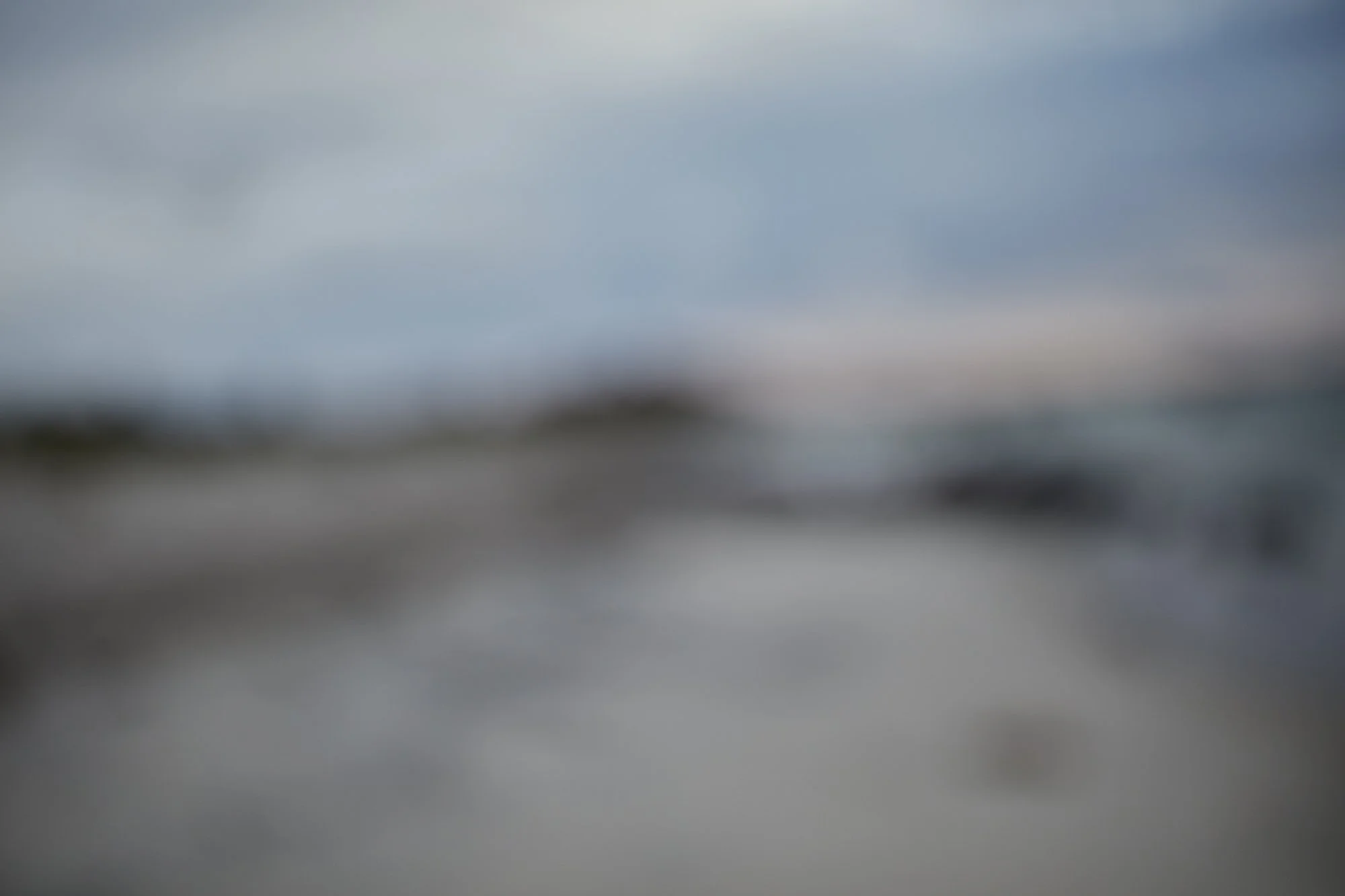 Blurred image of a cloudy sky over a body of water with indistinct objects or land in the foreground.
