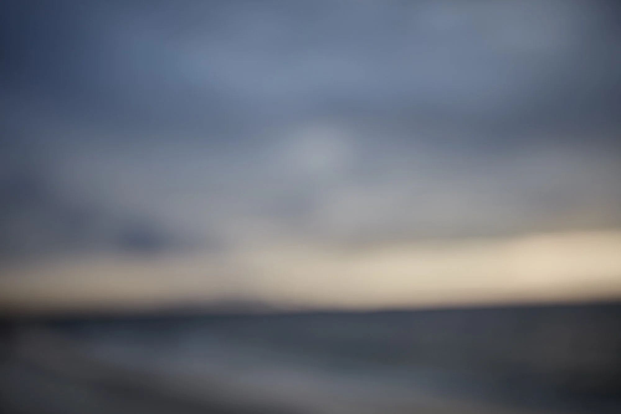 Blurred image of a landscape with a sky and horizon, showing a gradient of dark and light colors.