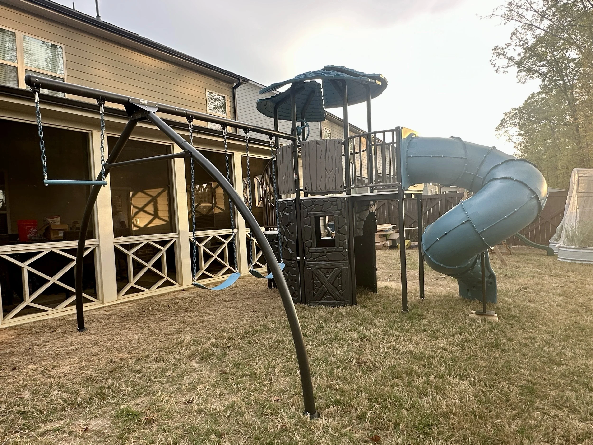Multi-feature backyard playset assembled with swings, elevated platforms, climbing areas, and a large spiral tube slide.