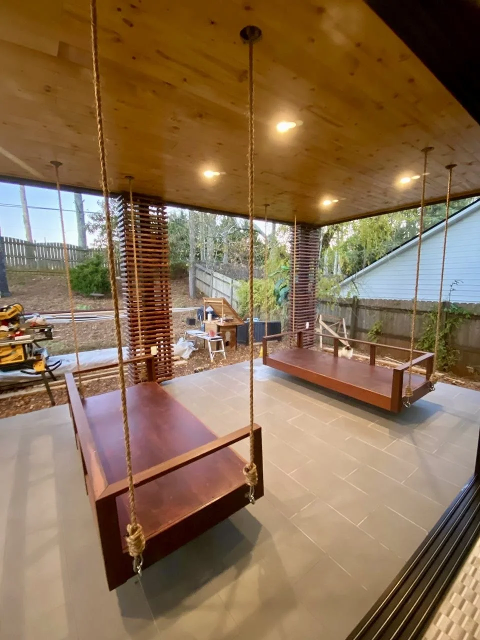 Covered outdoor living area featuring a wood-paneled ceiling, recessed lighting, decorative privacy screens, and custom hanging porch swings.