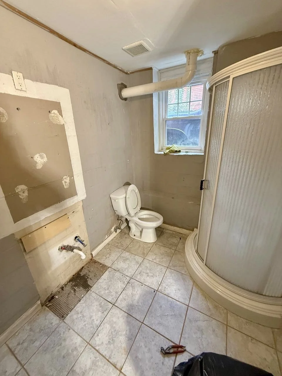 Before photo showing the original bathroom layout, flooring, fixtures, and shower enclosure prior to a complete remodel.