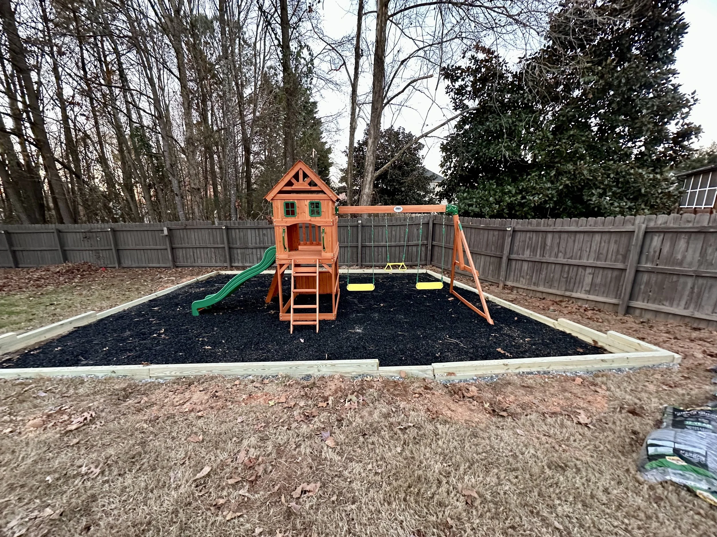 Wooden playset assembled over a bordered playground area with rubber mulch, creating a dedicated backyard space for safe outdoor play.