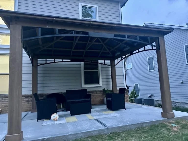 Large wood-frame gazebo assembled over an existing patio to create a shaded outdoor seating and entertaining area.