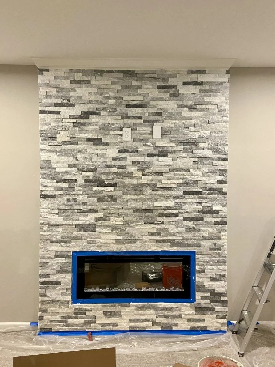 Floor-to-ceiling stacked-stone installation transforms a modern electric fireplace into a dramatic focal point.