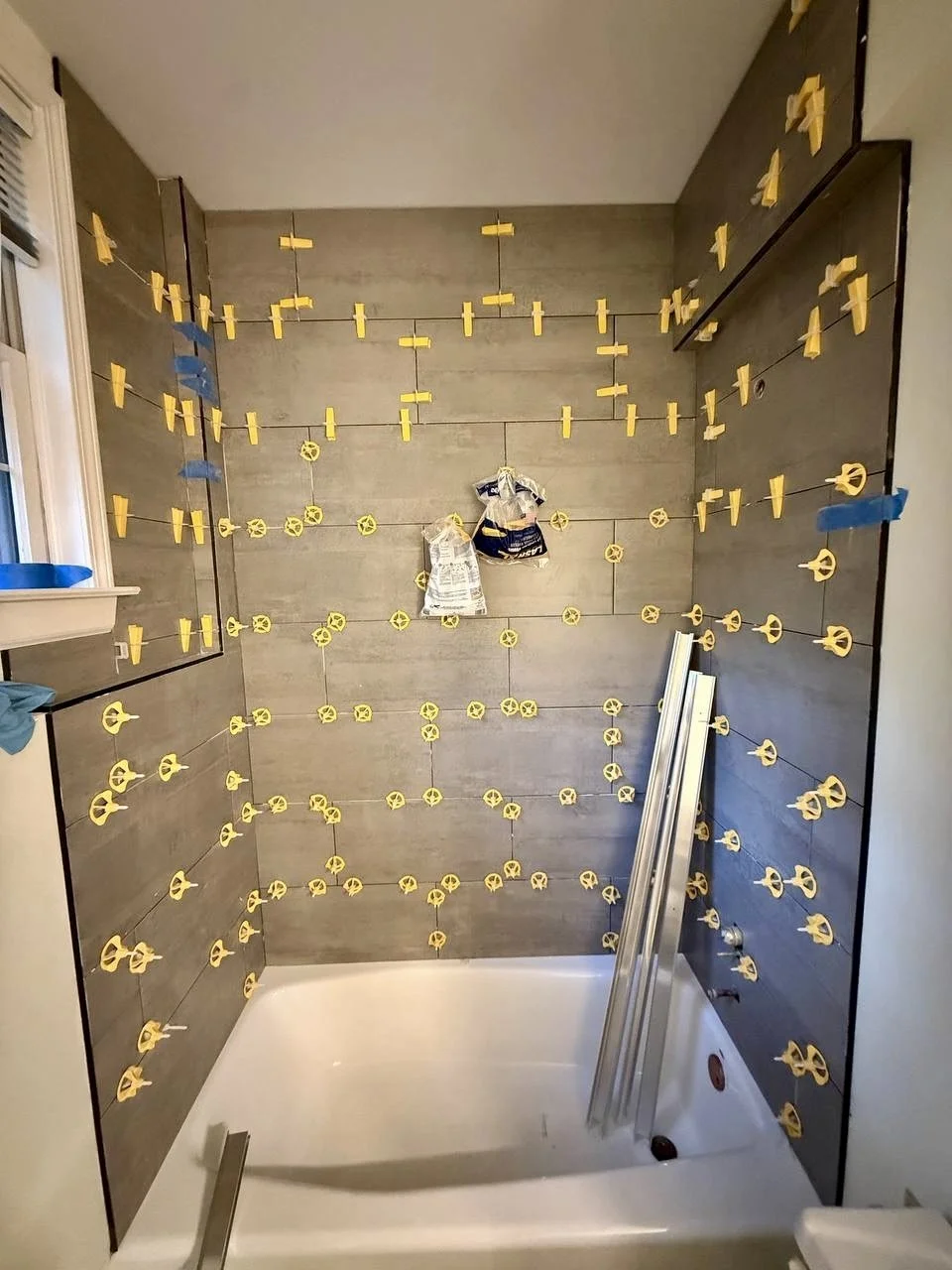 In-progress view showing careful tile spacing and leveling during installation of a full tub and shower surround.
