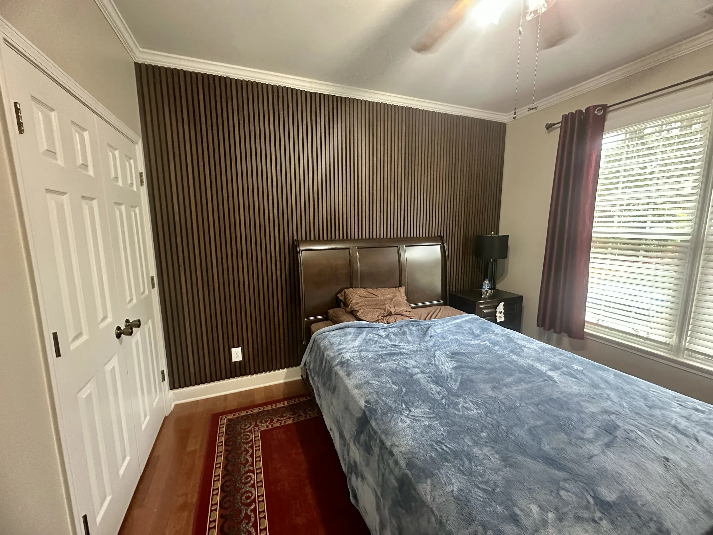 Finished floor-to-ceiling wood slat feature wall creating a polished focal point behind the bed.