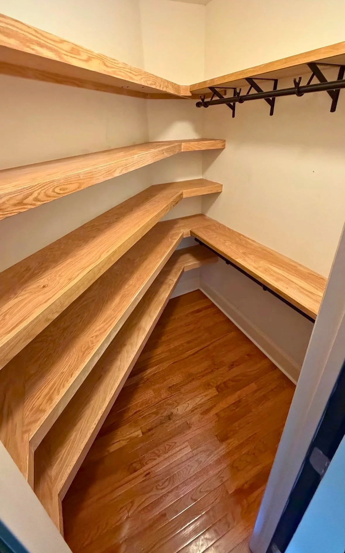 Custom-built natural wood shelving and hanging rods designed to maximize storage throughout a walk-in closet.