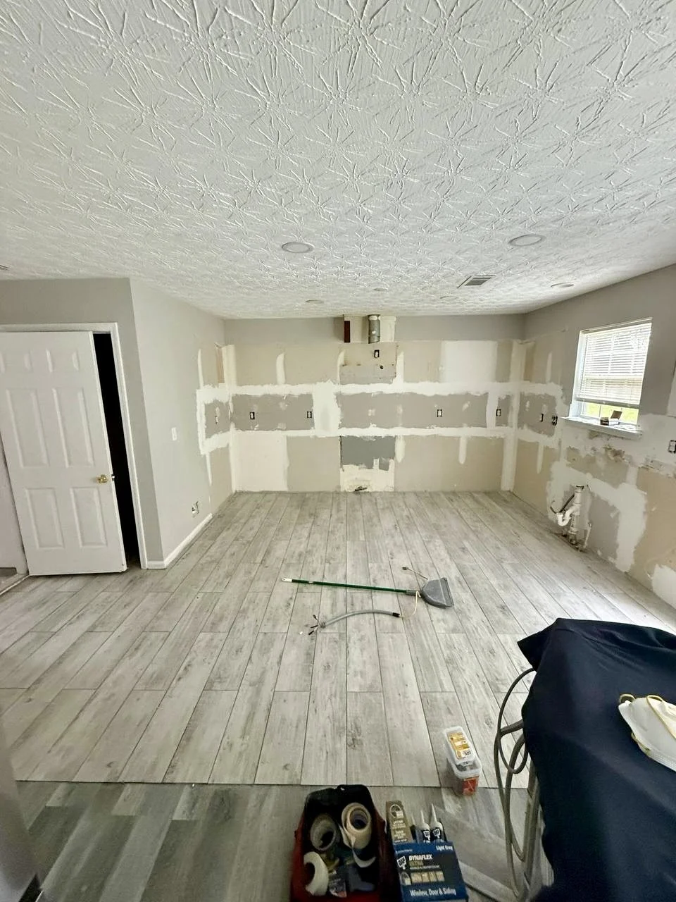 Kitchen remodel in progress with new wood-look tile flooring installed and walls prepared for cabinetry and finishes.