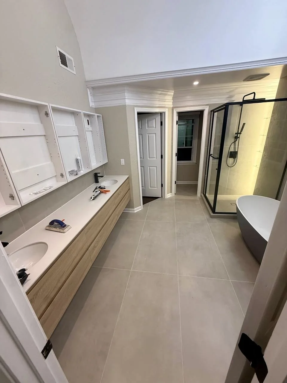 Spacious bathroom renovation featuring a floating double vanity, large-format flooring, freestanding tub, and glass-enclosed shower.