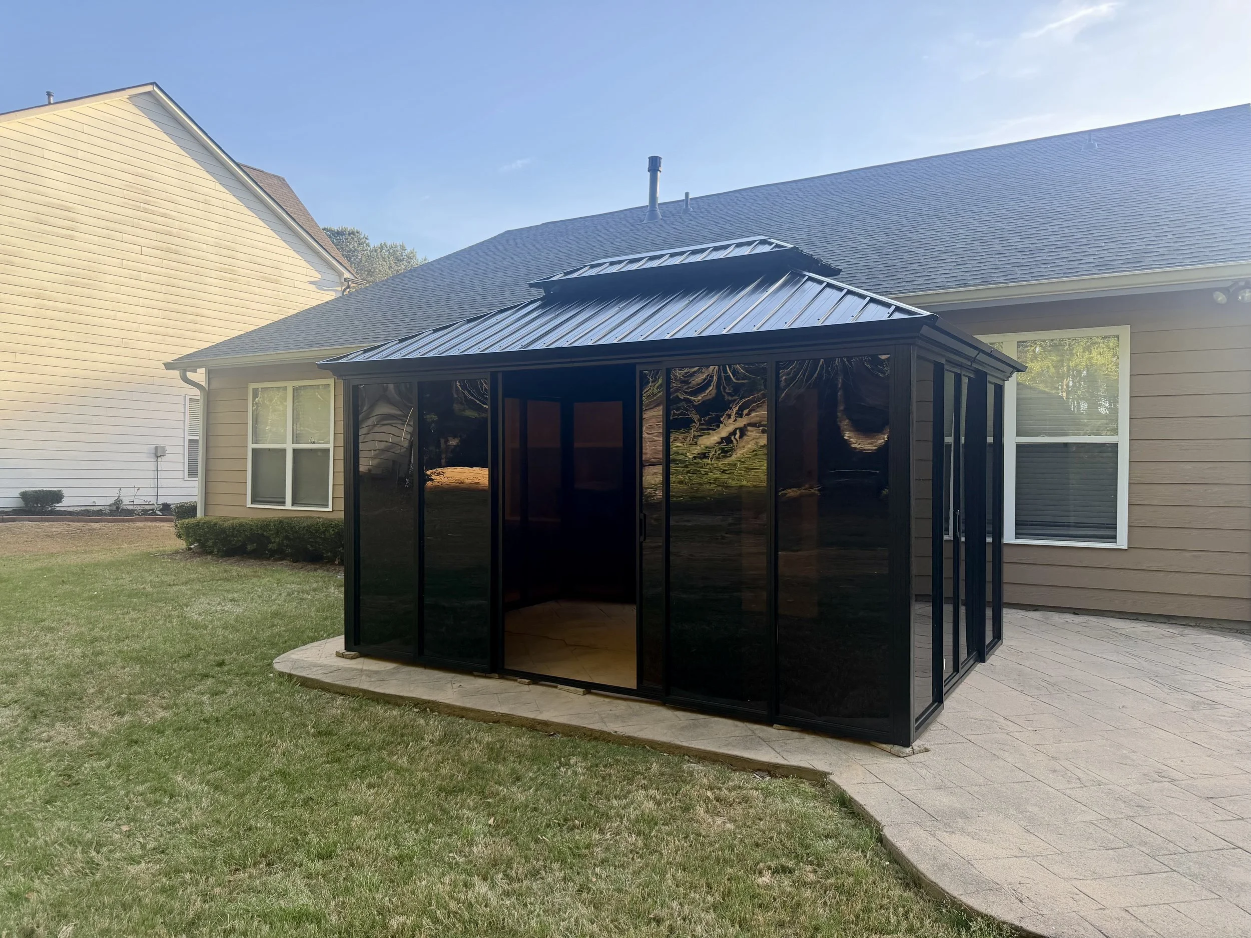Fully enclosed metal-roof gazebo assembled on an existing patio to create a protected outdoor living and entertaining space.