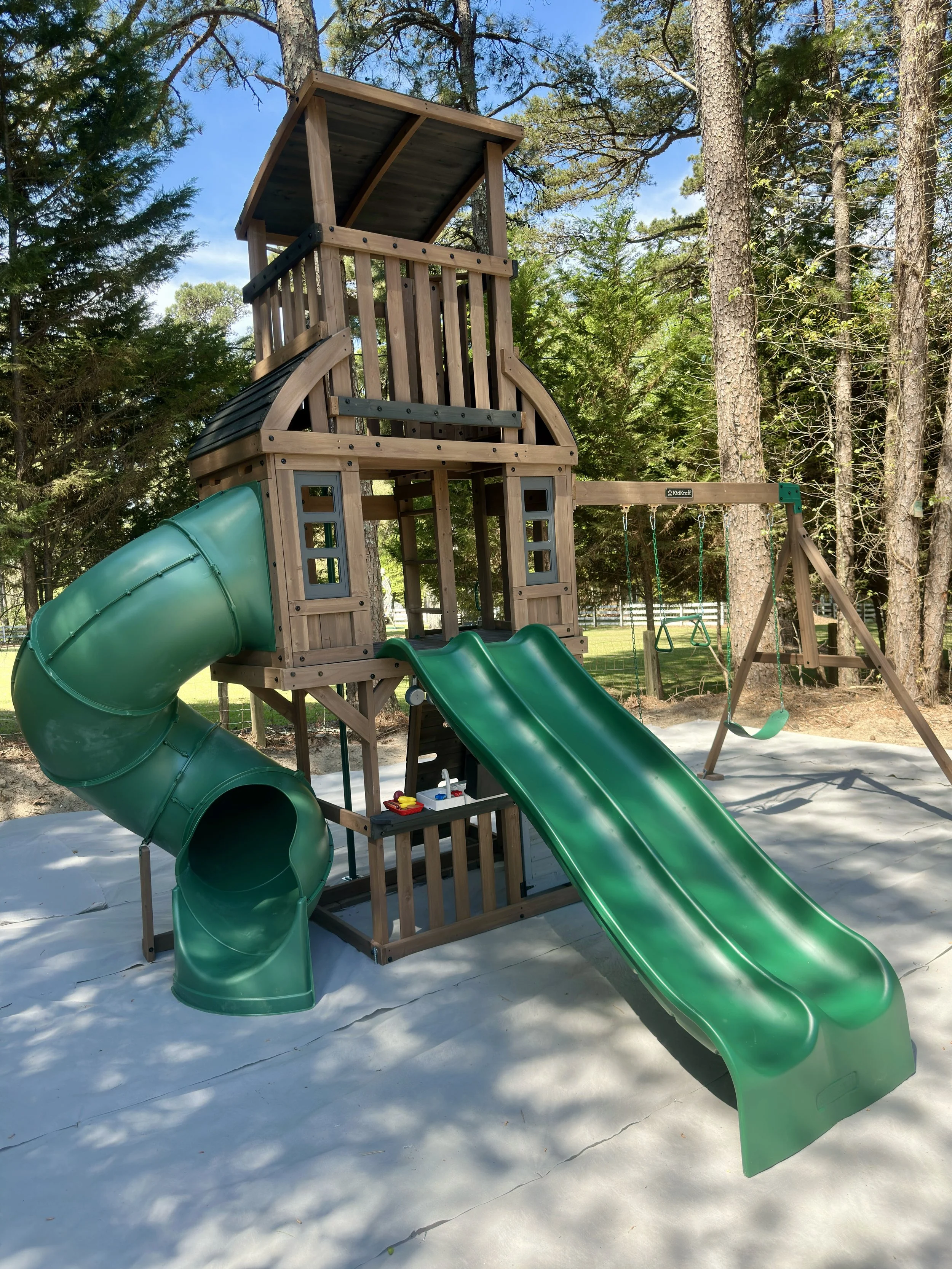 Large wooden playset assembled with a tower, covered upper level, double slide, tube slide, climbing features, and attached swings.