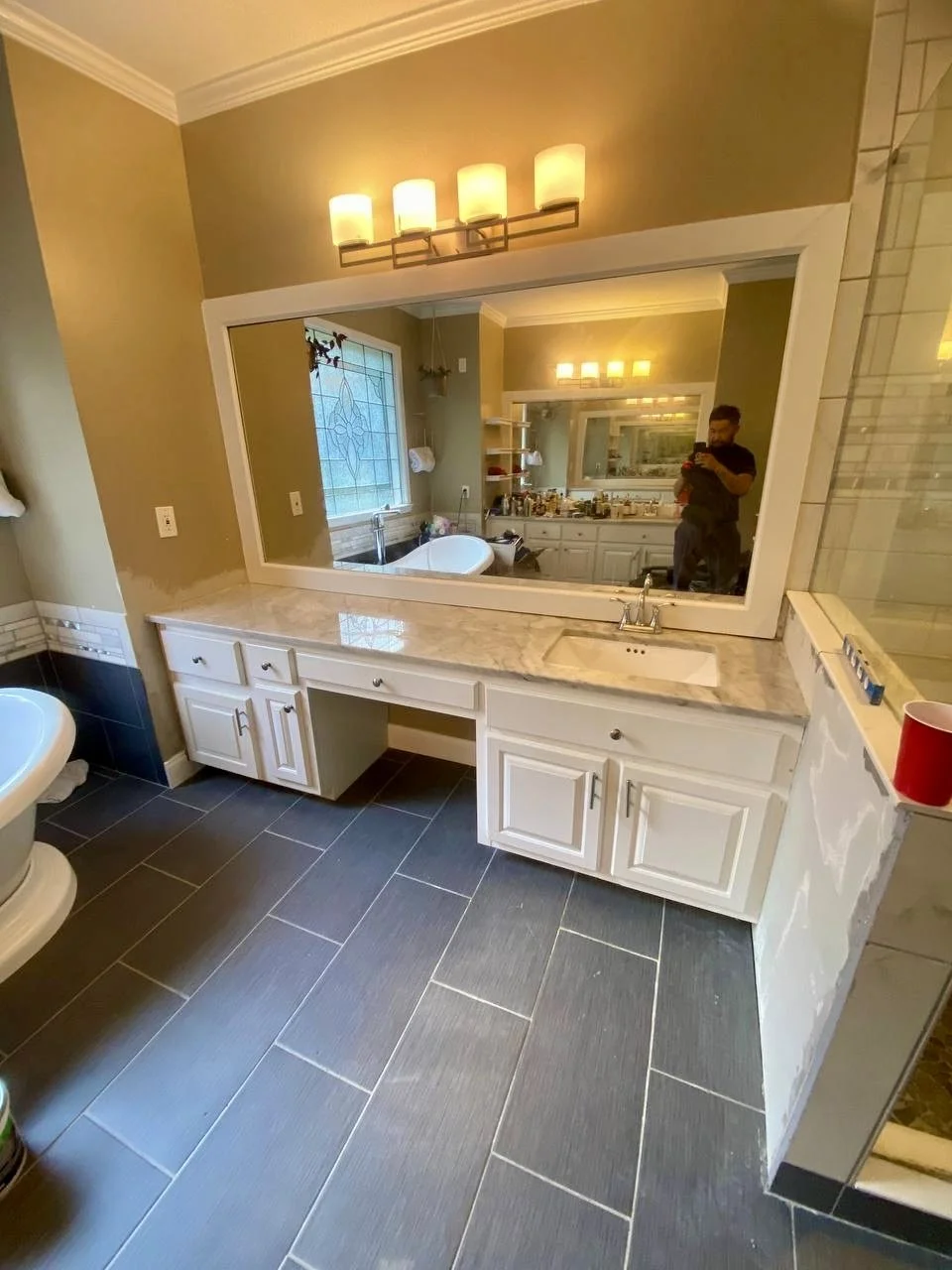 Spacious double vanity with stone countertop, oversized framed mirror, updated lighting, cabinetry, and dark tile flooring.