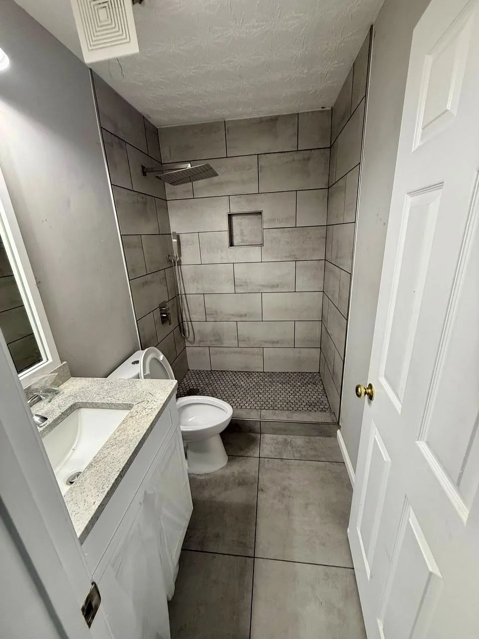 Updated bathroom with large-format gray tile, mosaic shower floor, built-in niche, rainfall showerhead, and streamlined walk-in design.