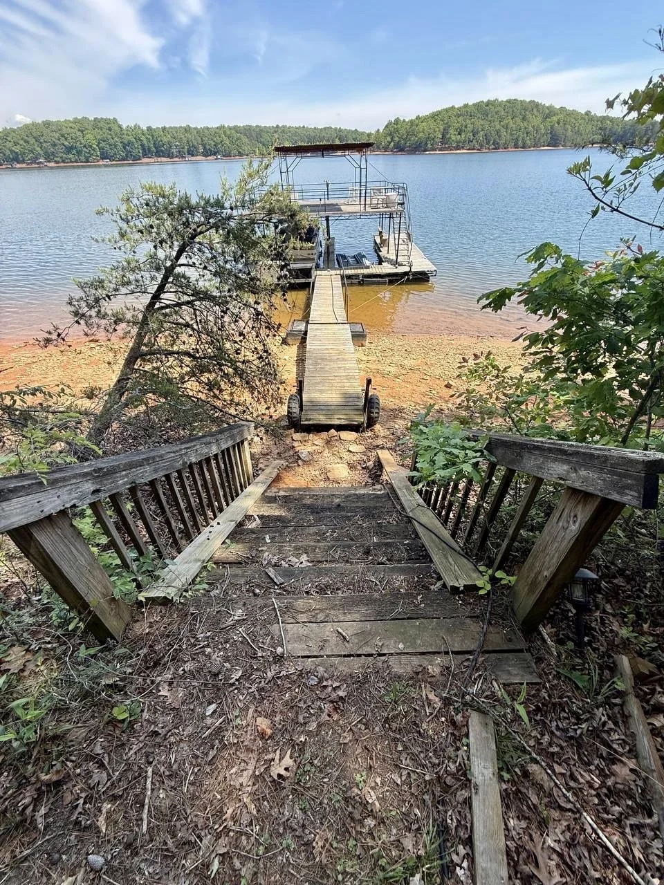 Before view showing the deteriorated wooden stairway leading down the slope toward the lake and dock.