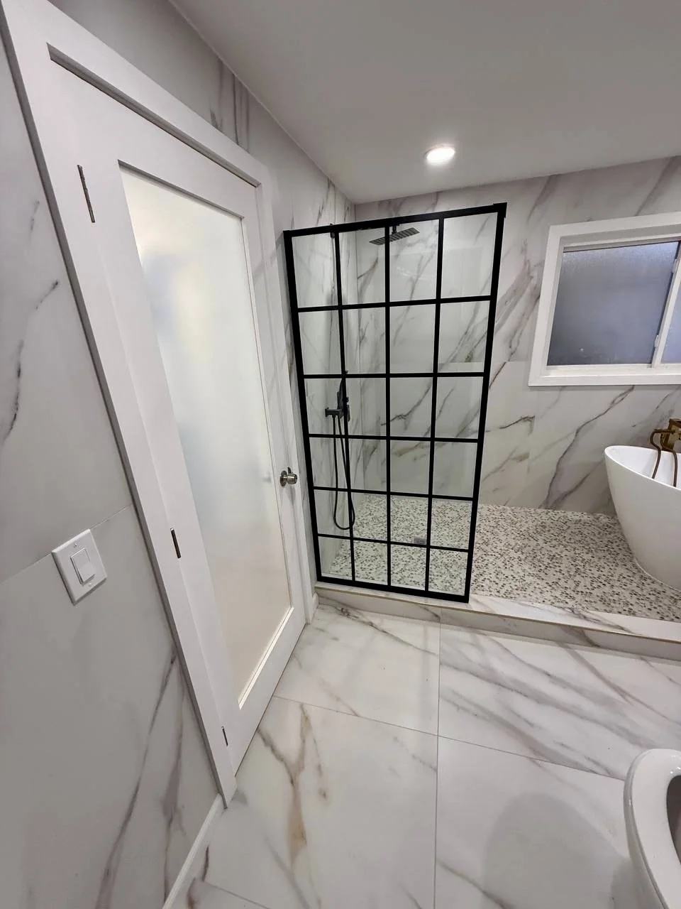 Floor-to-ceiling marble-look tile and a black grid-style glass partition create a bright, upscale wet-room design.