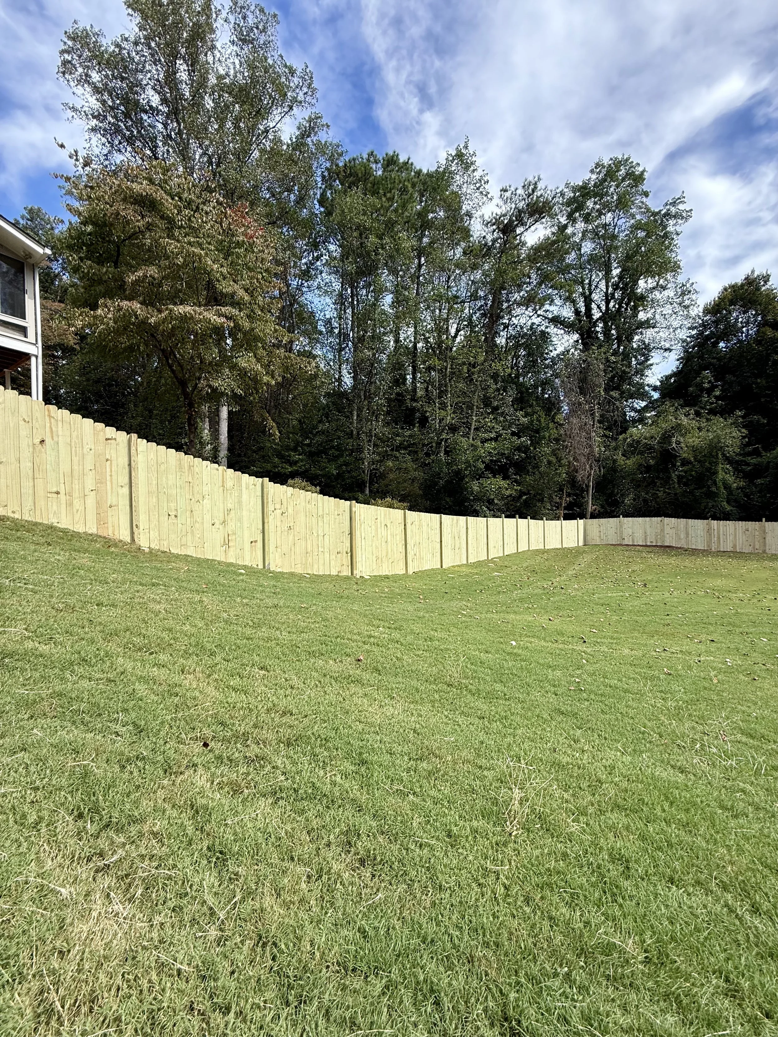 Newly installed wood privacy fencing encloses a large backyard while maintaining a clean, consistent appearance across changing terrain.