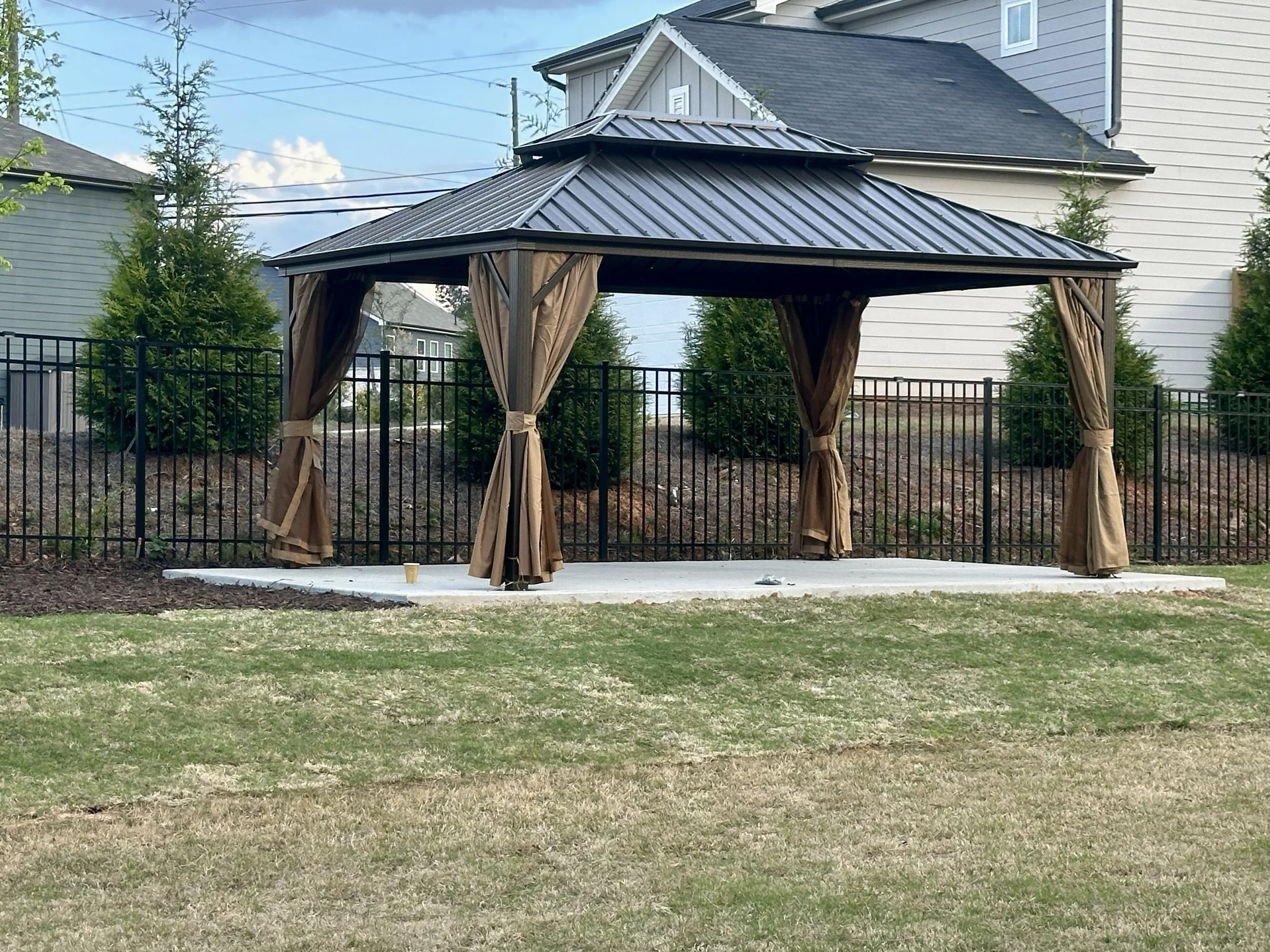 Large freestanding gazebo assembled on a concrete pad with a durable metal roof and curtains for shade and privacy.
