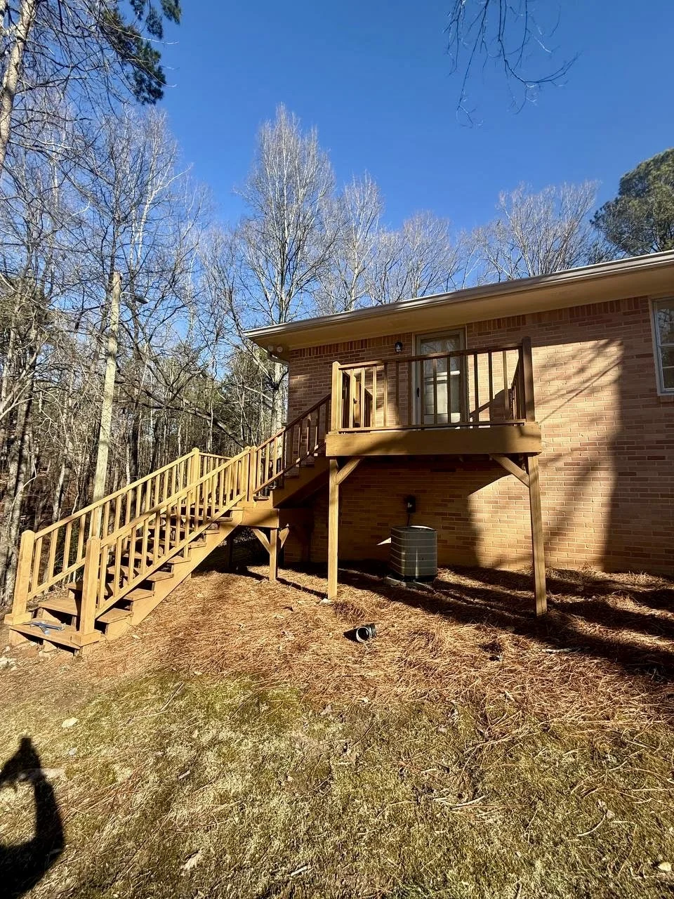 Finished exterior staircase and landing with sturdy wood railings, providing secure access from the backyard to the upper-level entrance.