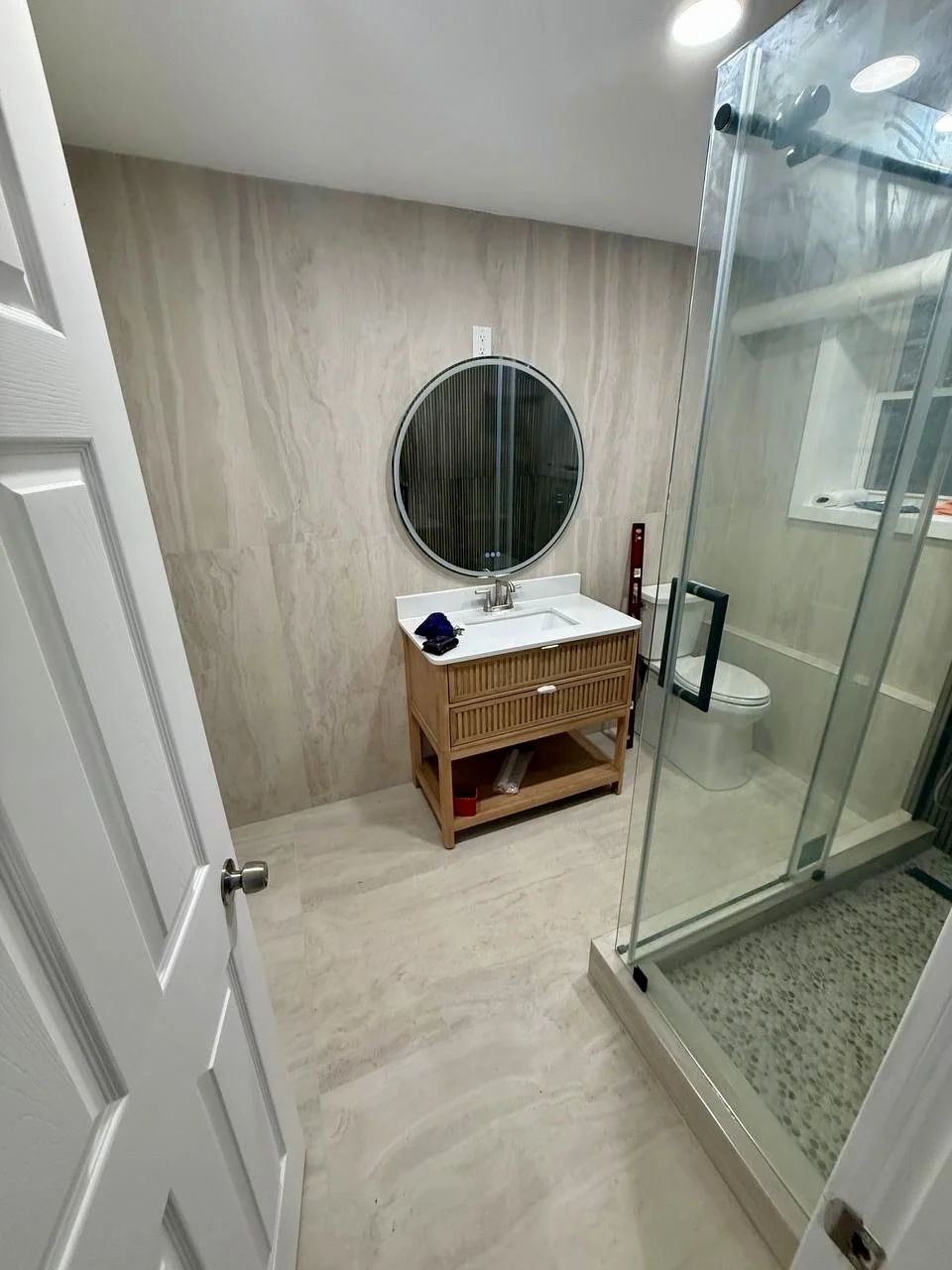 Contemporary bathroom finished with coordinated stone-look wall and floor surfaces, wood vanity, and glass-enclosed shower.