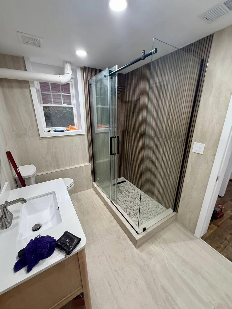 Glass-enclosed shower featuring textured vertical wall tile, pebble-style flooring, and contrasting black hardware.