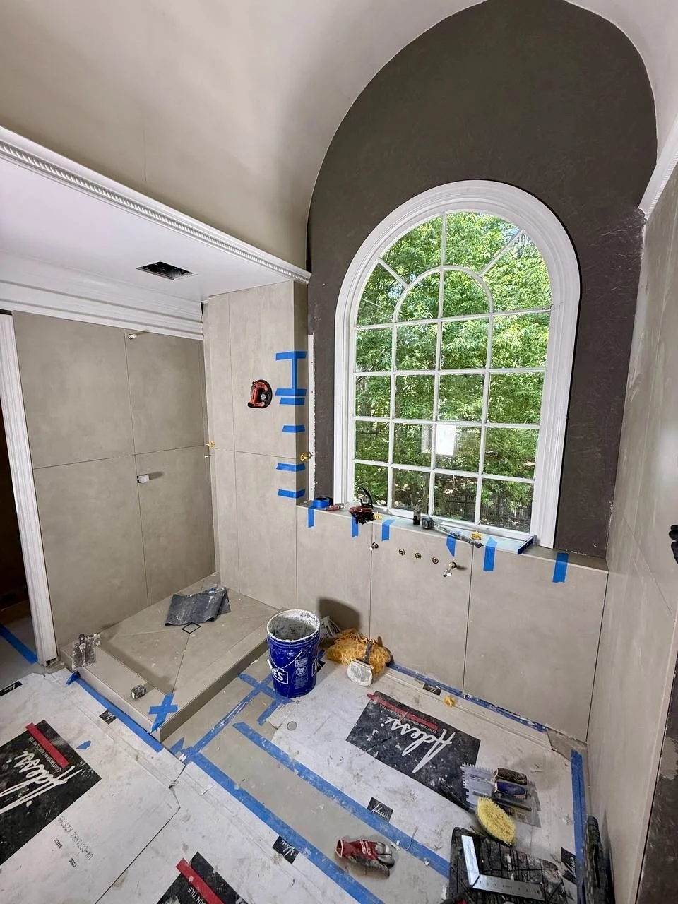 Large-format tile installation around a custom shower and statement arched window during a full bathroom remodel.