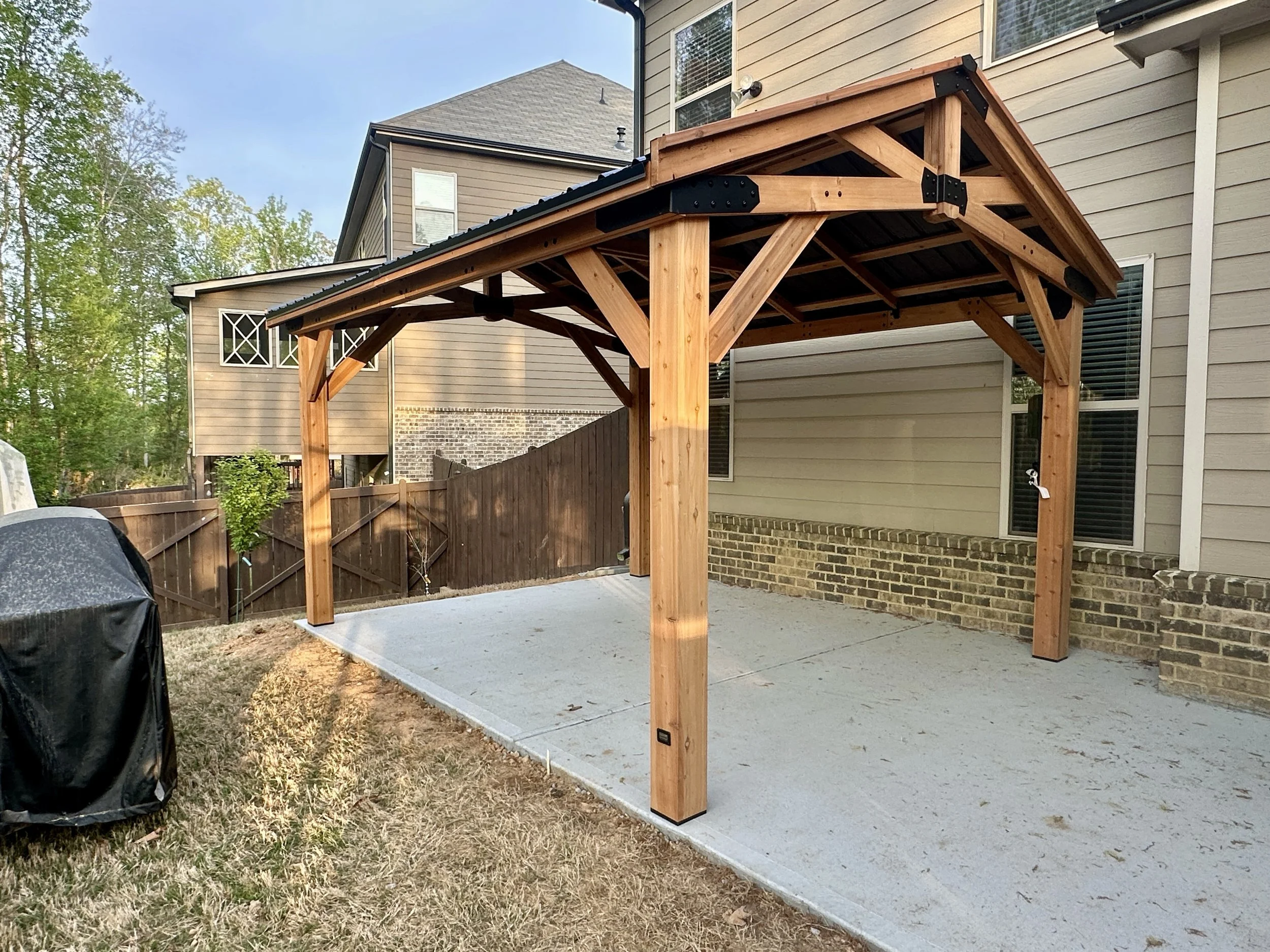 Cedar gazebo assembled on an existing concrete patio, featuring heavy timber construction and a durable metal roof.