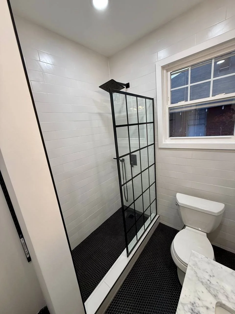 Classic white wall tile paired with black mosaic flooring, matte black fixtures, and a grid-style glass shower panel.