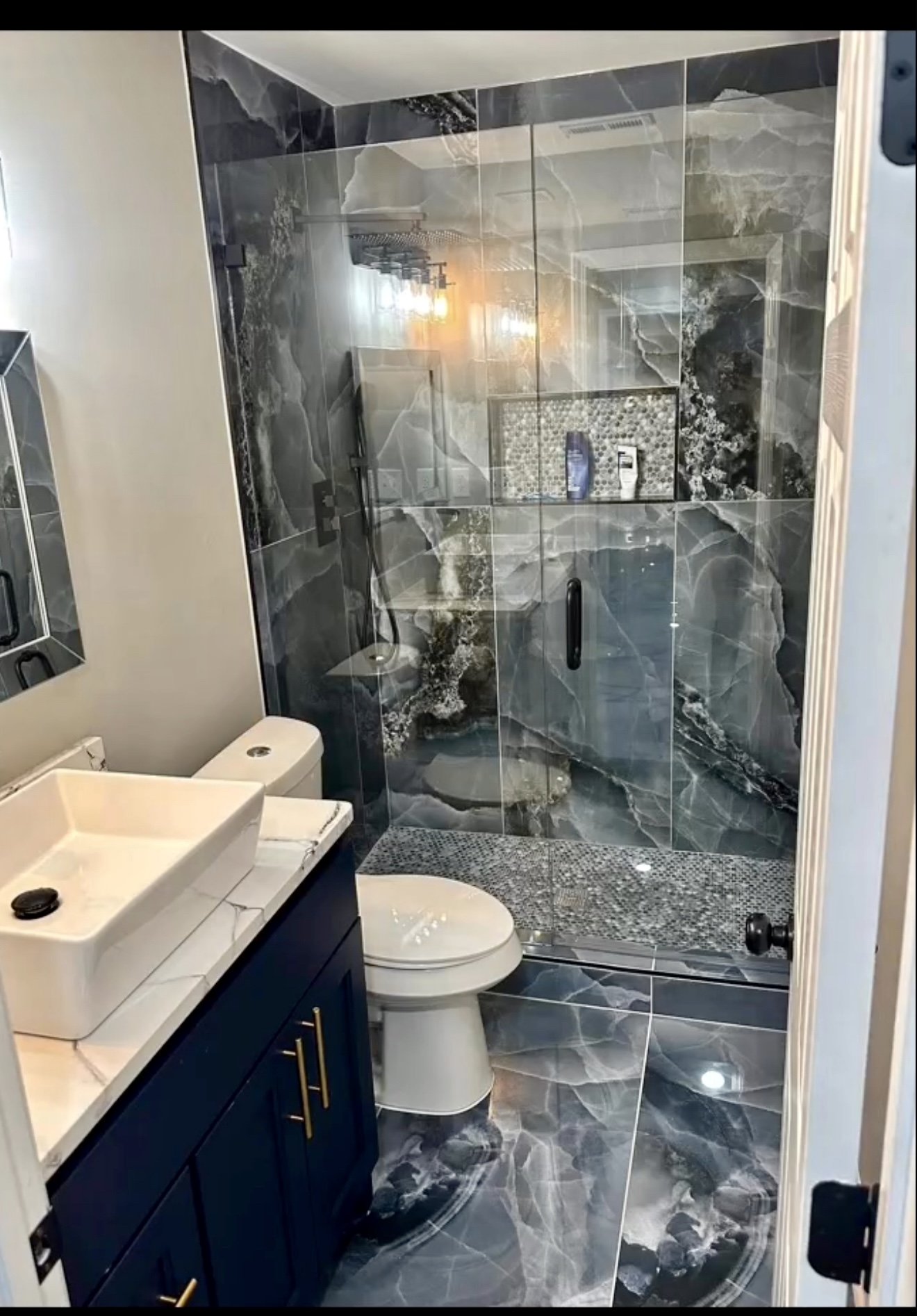 Bold marble-look tile, mosaic shower flooring, glass enclosure, and modern fixtures create a dramatic contemporary bathroom.