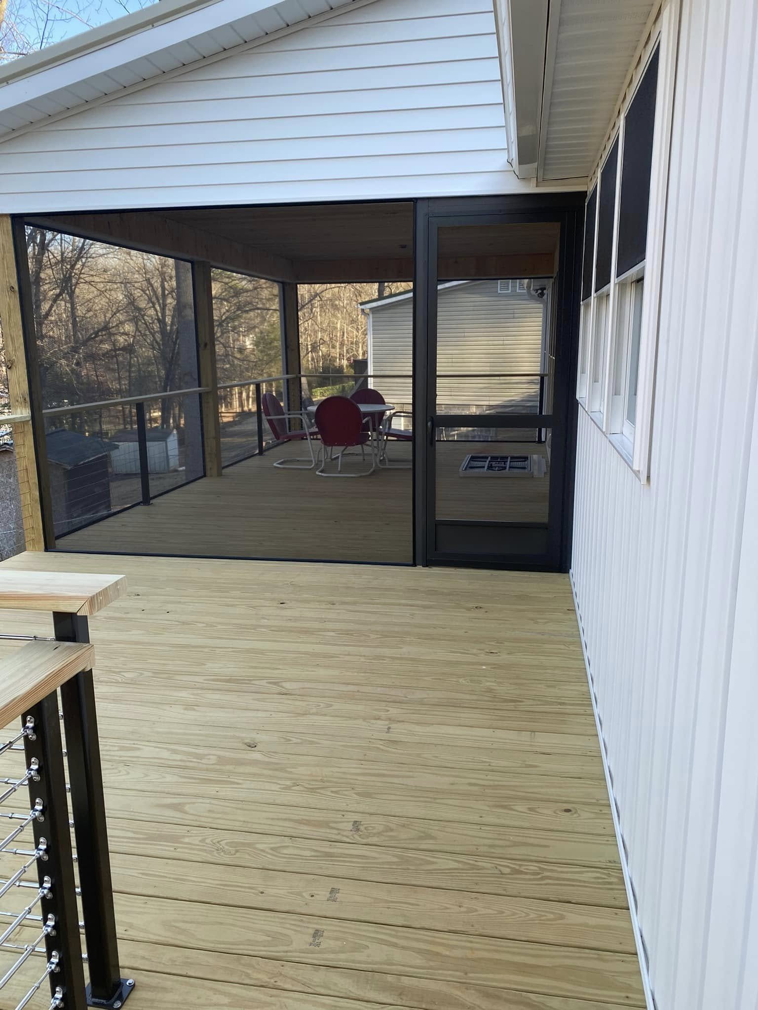 Newly constructed wooden deck attached to a house, with a screened-in porch area and a sitting table with three chairs. Trees are visible in the background.