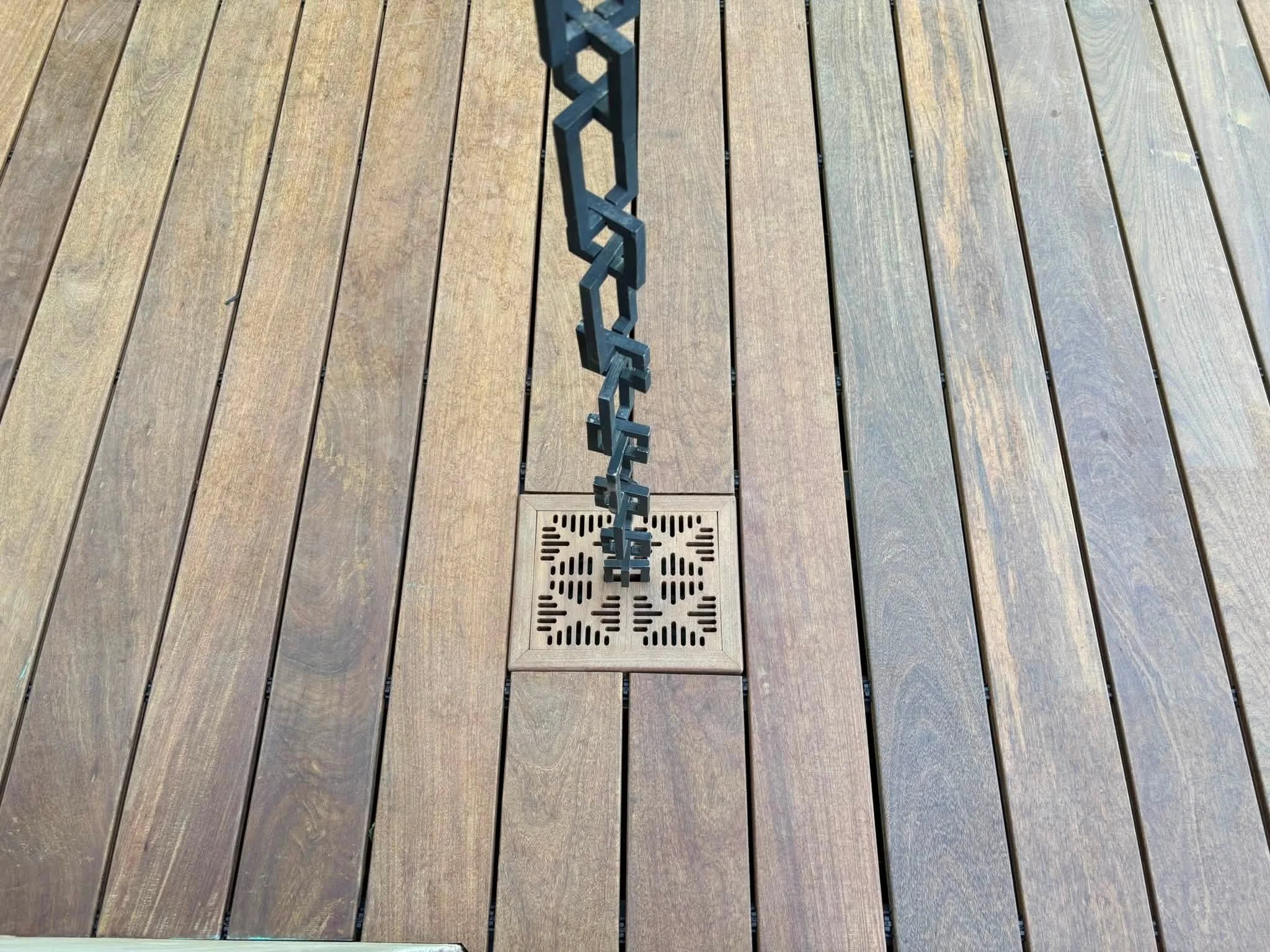 wooden deck with a floor drain and a metal chain with paperclips hanging from it.
