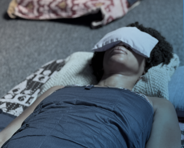 Person lying on a bed with a blanket, with their face covered by a pillow.