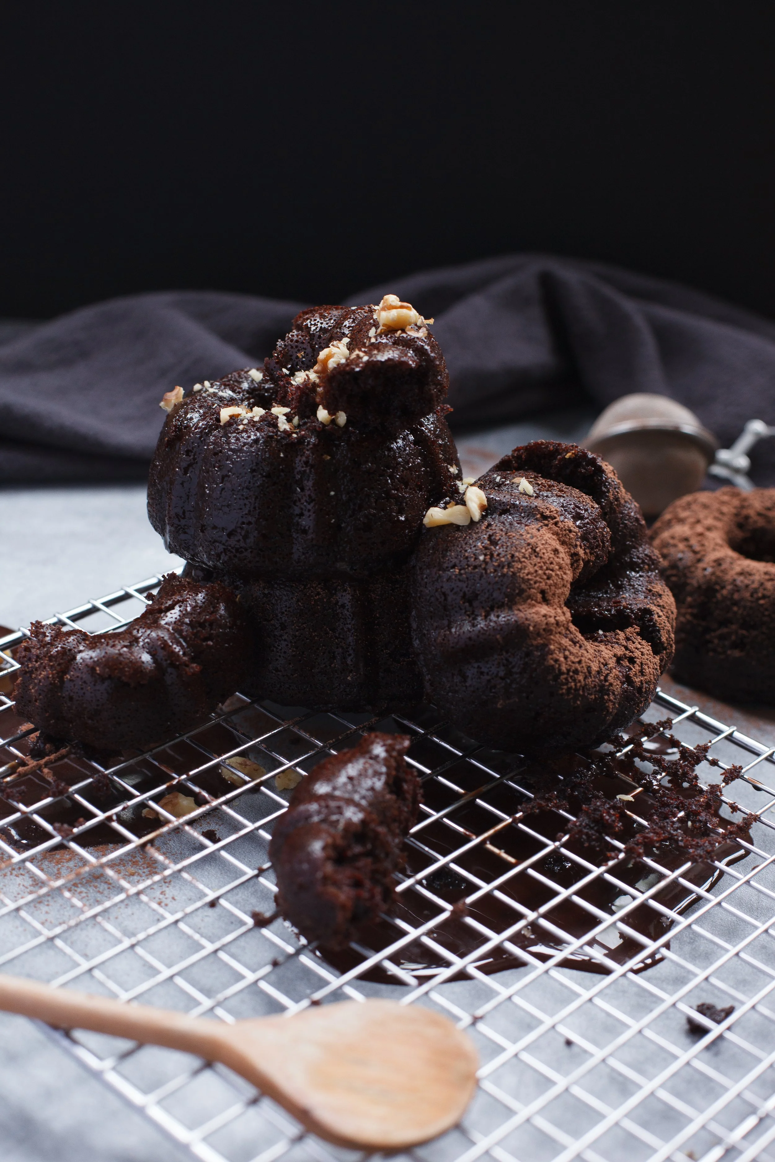 Chocolate baked goods, possibly crinkle cookies, on a wire cooling rack with a wooden spoon in the foreground.