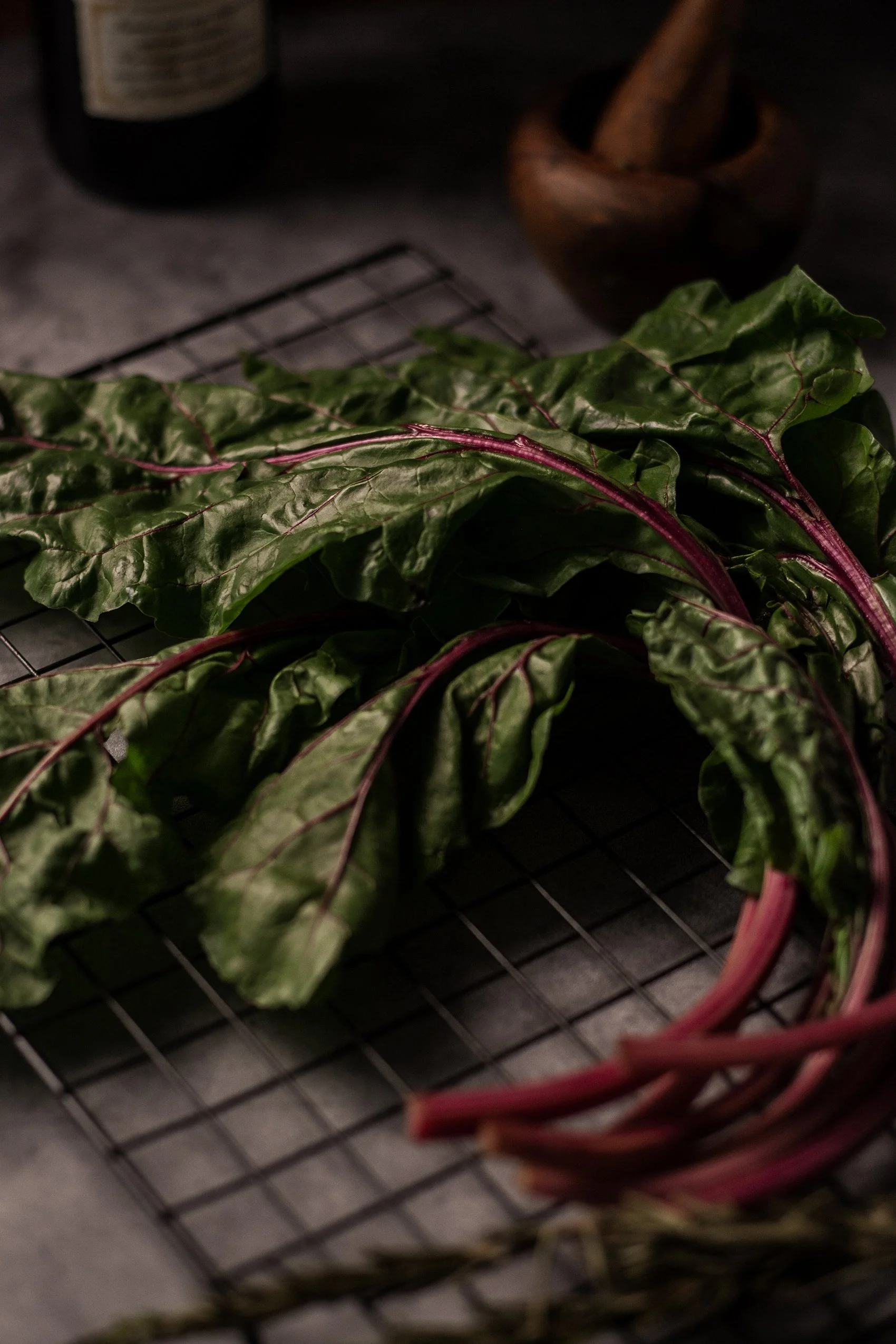 Fresh leafy greens with purple stems on a wire rack.