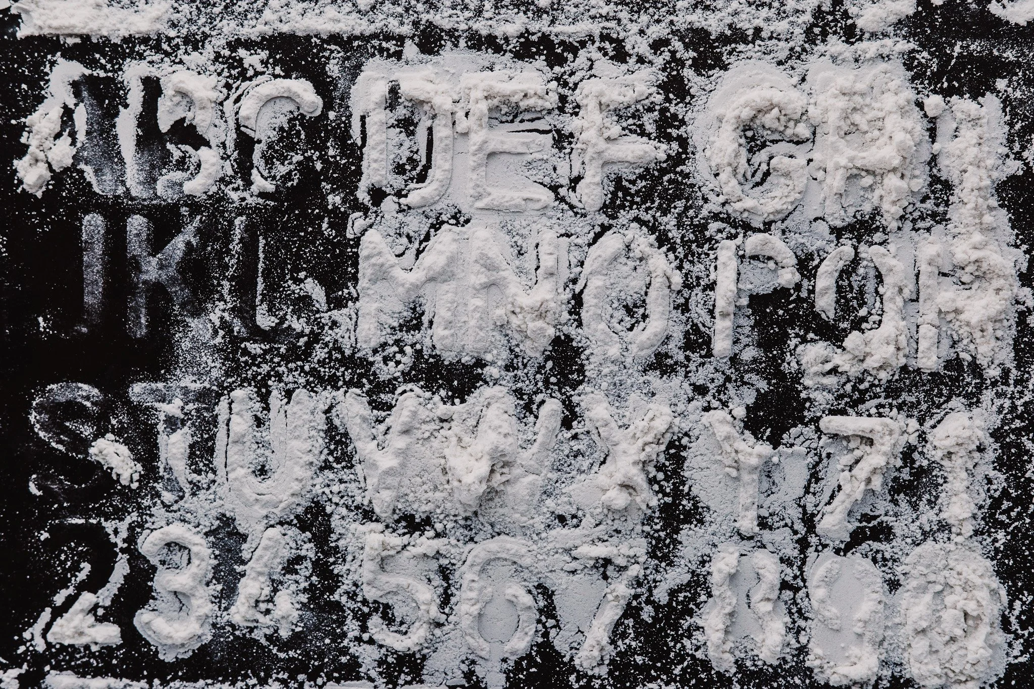 The alphabet is stenciled in flour on a black surface.