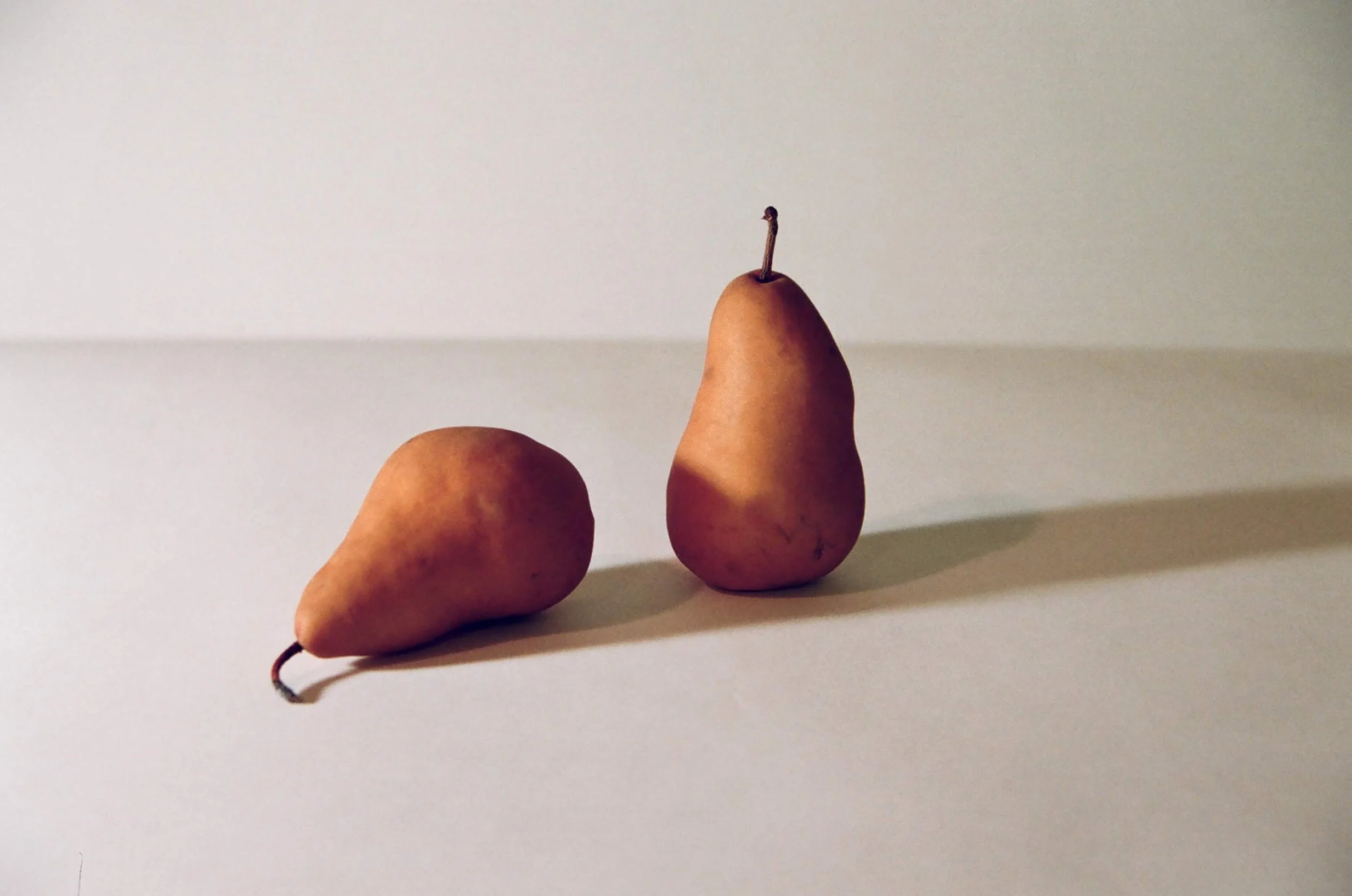 Two pears on a white surface with a plain light-colored background.