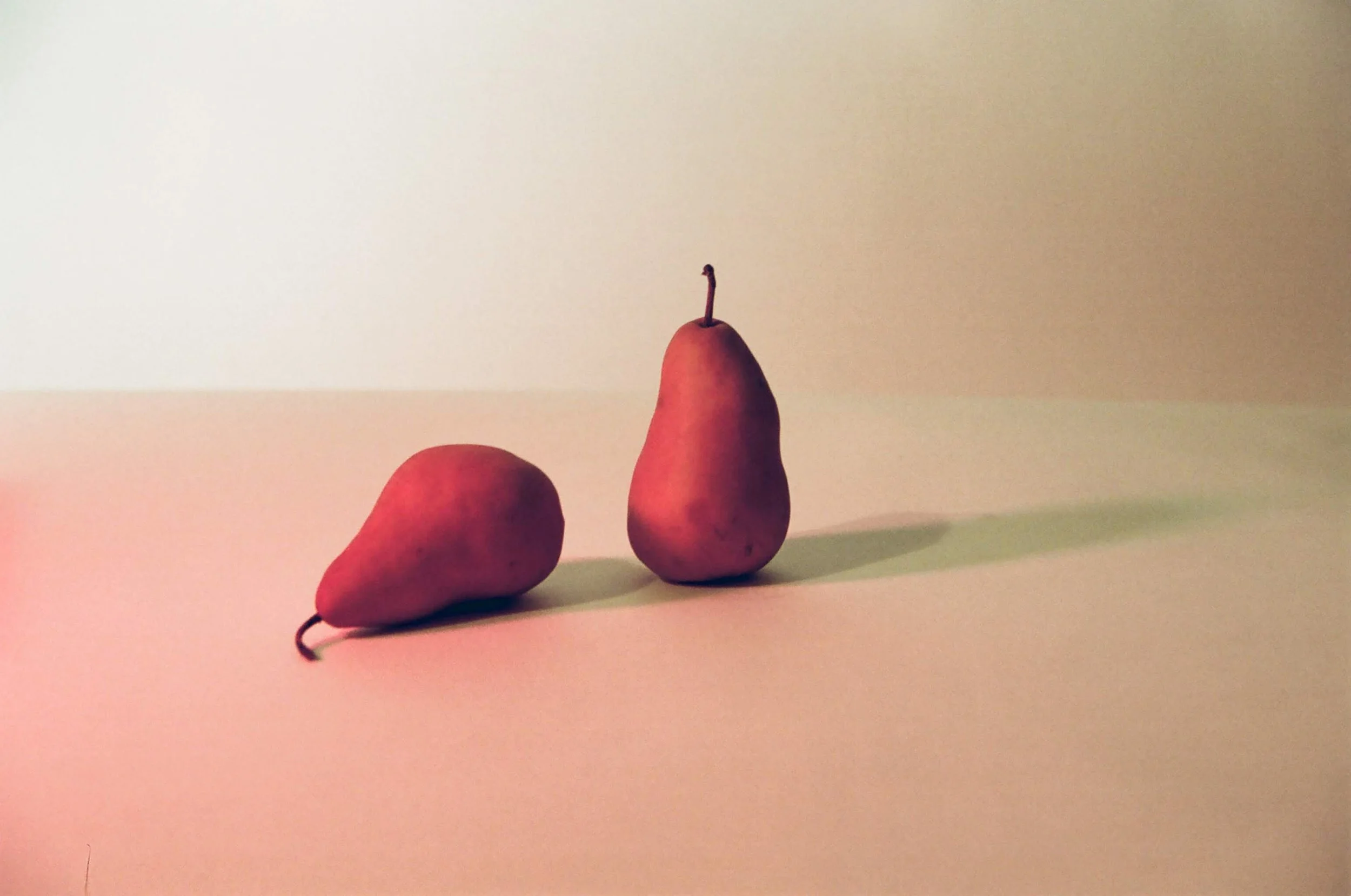 Two small pears on a flat surface, with one pear standing upright and the other leaning against it.