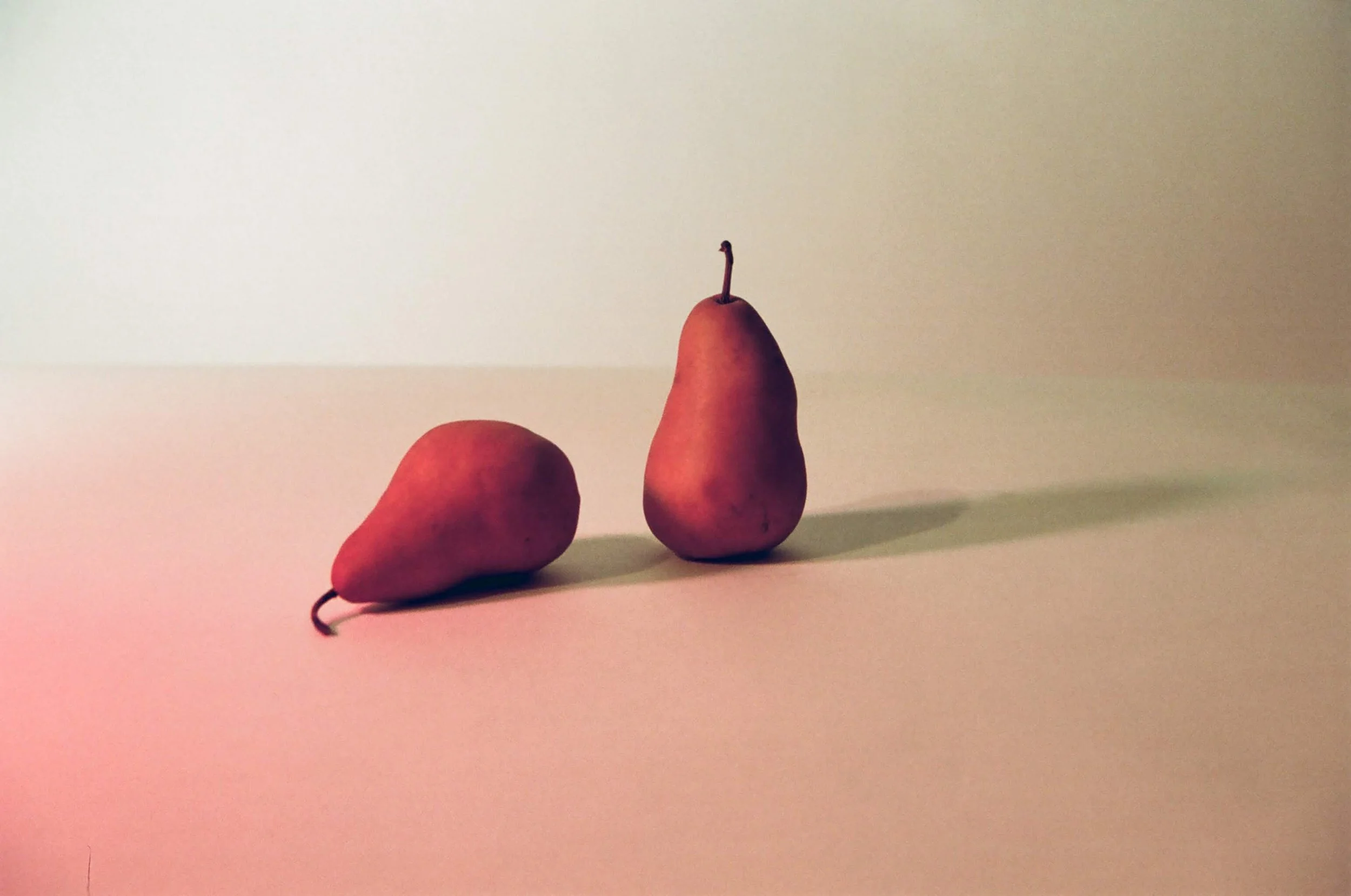 Two pears placed on a flat surface with a plain light background, one pear slightly tilted and the other standing upright.