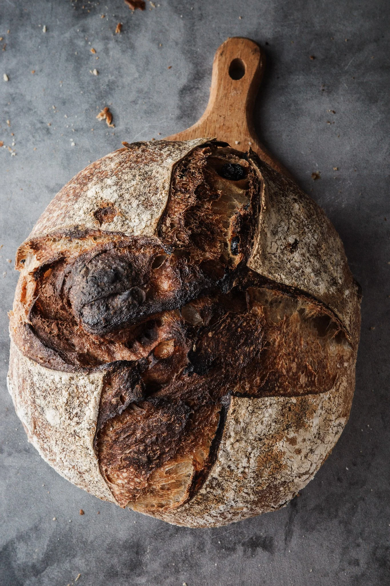 A rustic sourdough bread boule with a crusty, flour-dusted exterior, resting on a dark surface.