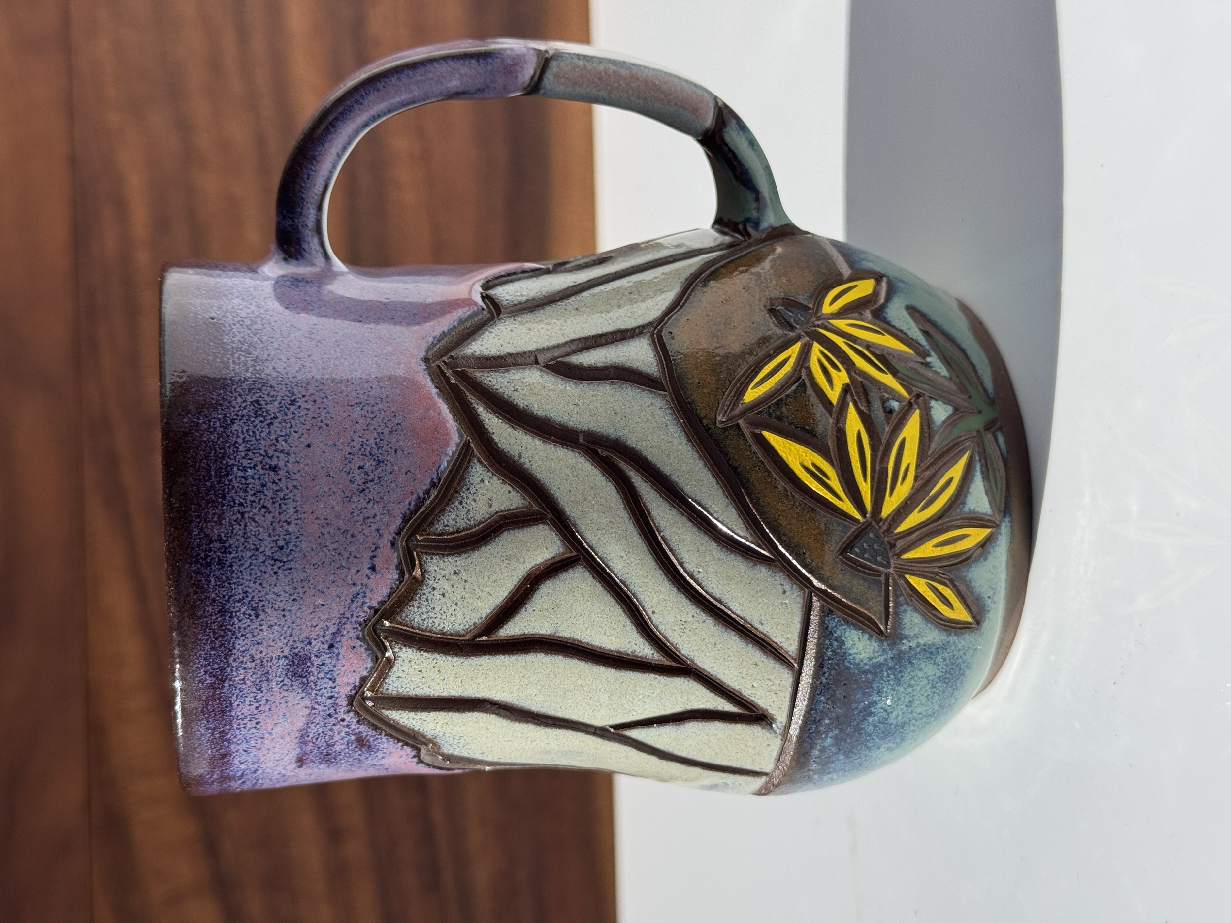Decorative ceramic mug with a yellow floral accent design, placed on a wooden surface with a wood background.