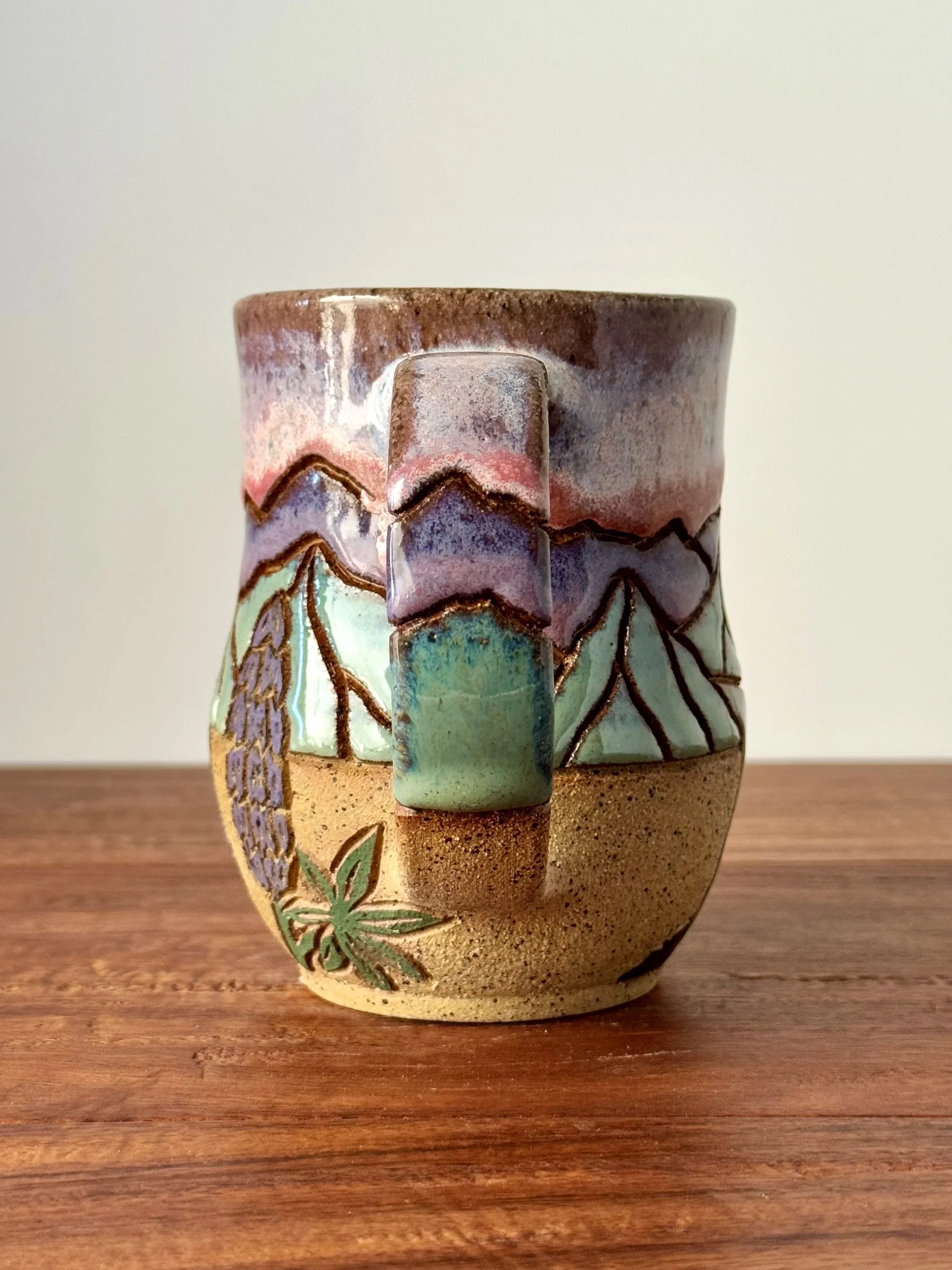 A ceramic mug with colorful glaze and leaf patterns, placed on a wooden surface.