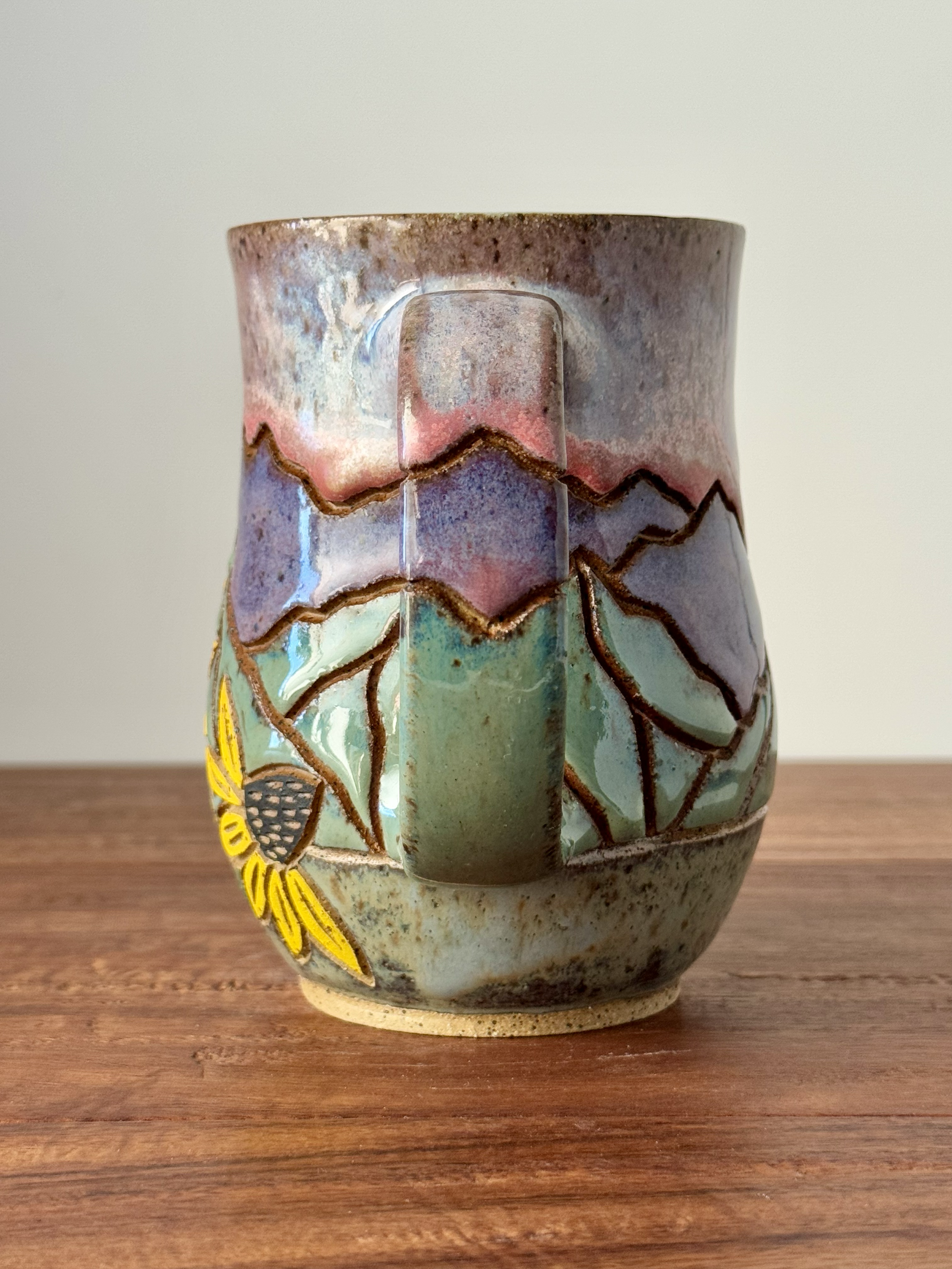 Ceramic mug with colorful, textured glaze featuring sunflower designs, placed on a wooden surface.
