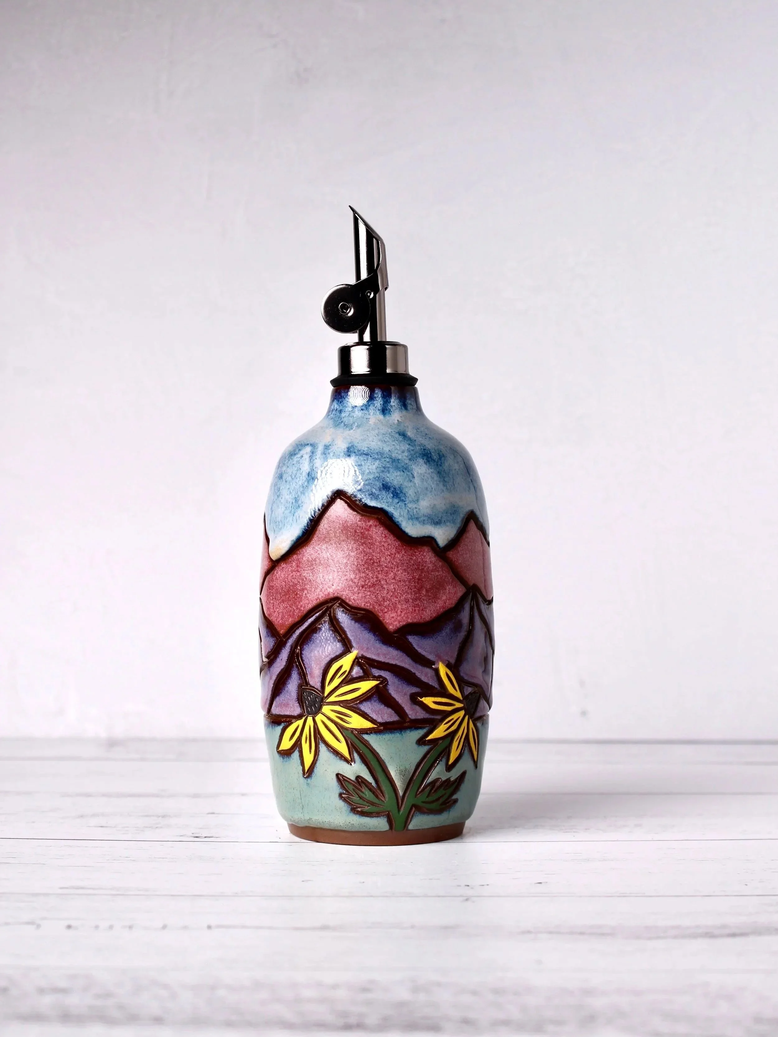 Colorful ceramic vase with hand-painted floral and mountain design, set on a white wooden surface against a plain white background.