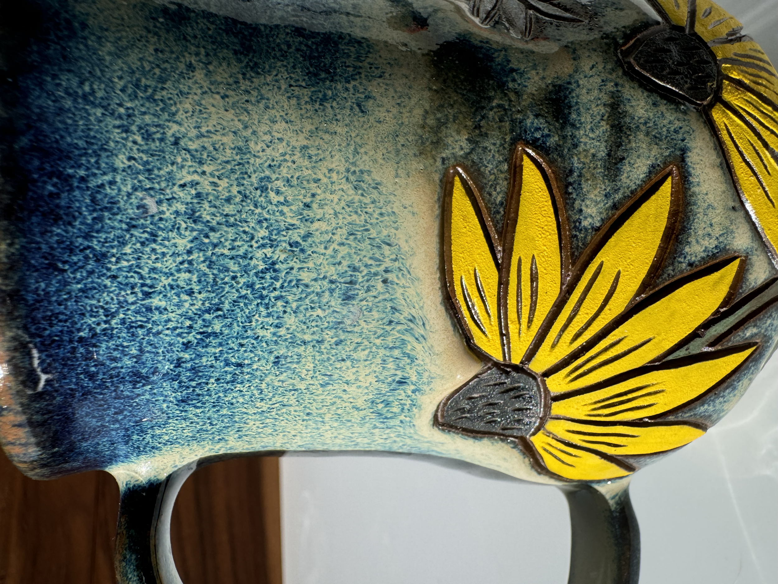 Close-up of a colorful ceramic sculpture featuring a yellow butterfly with black outlines and detailed wings, set against a blue and black textured background.