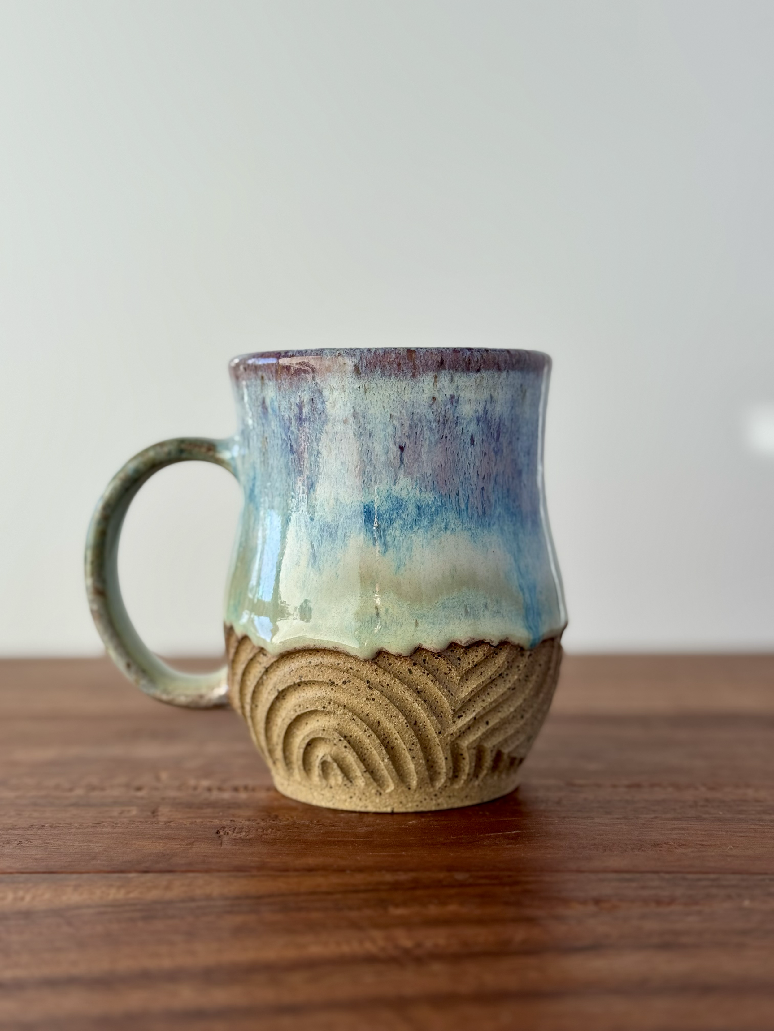 A ceramic mug with a colorful glaze on top of a wooden surface.