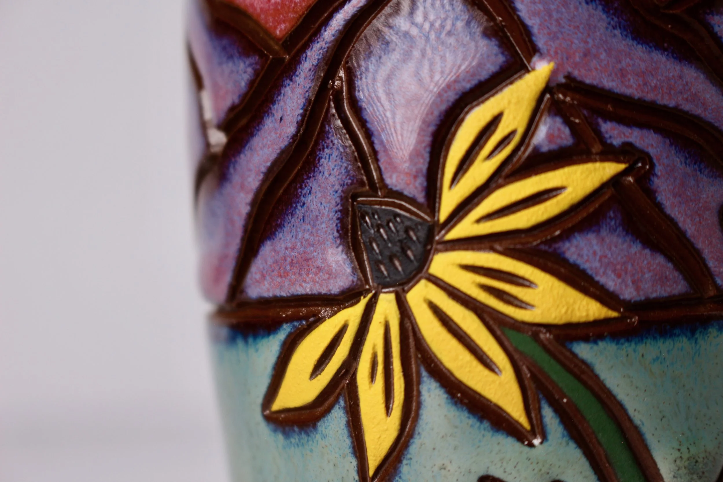 Close-up of a colorful black eye Susan flower painted on an oil pourer, with yellow, black, and brown details, and purple and pink glazes